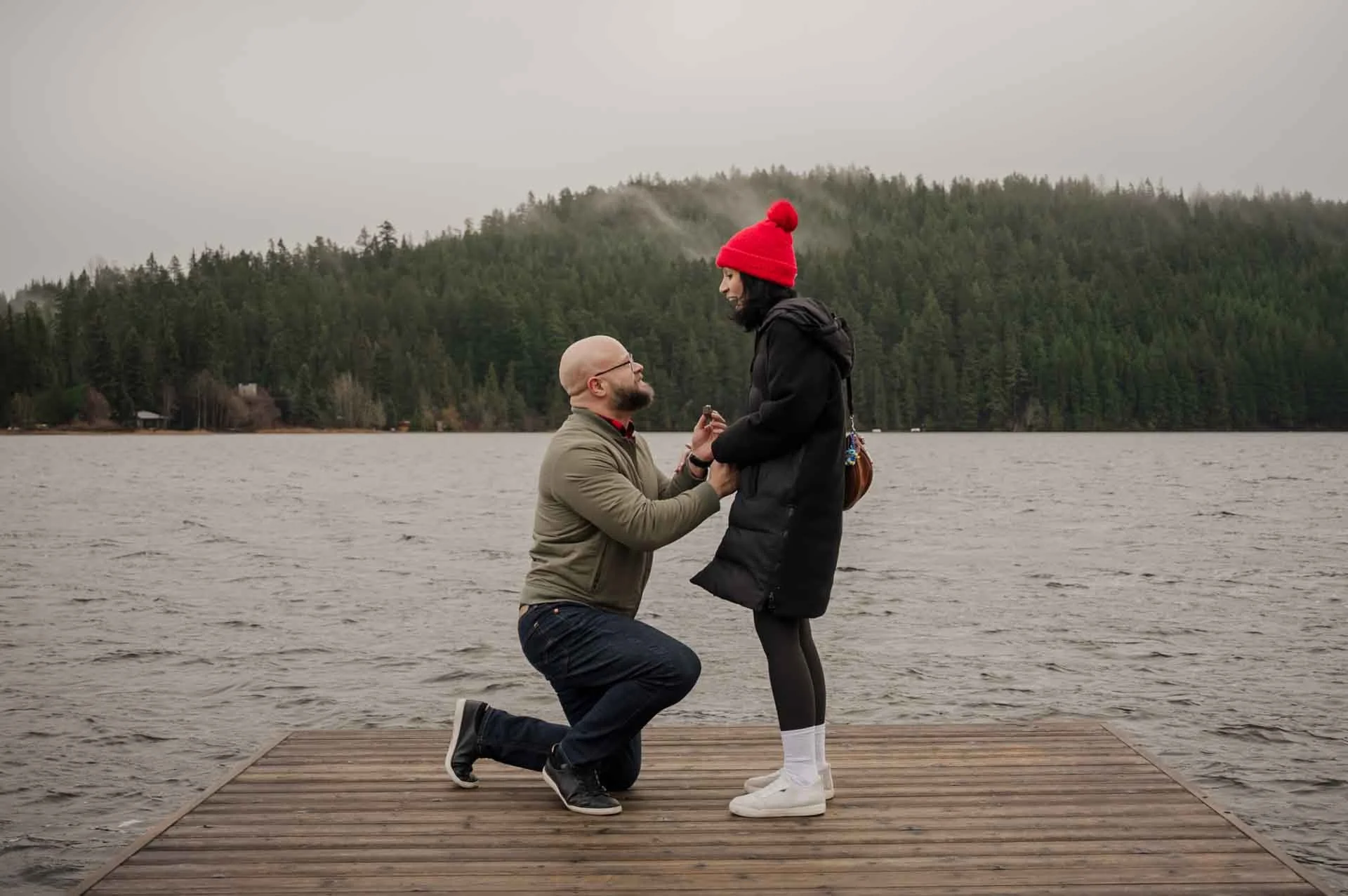man down on one know in front of a woman on a dock in front of a body of water and trees
