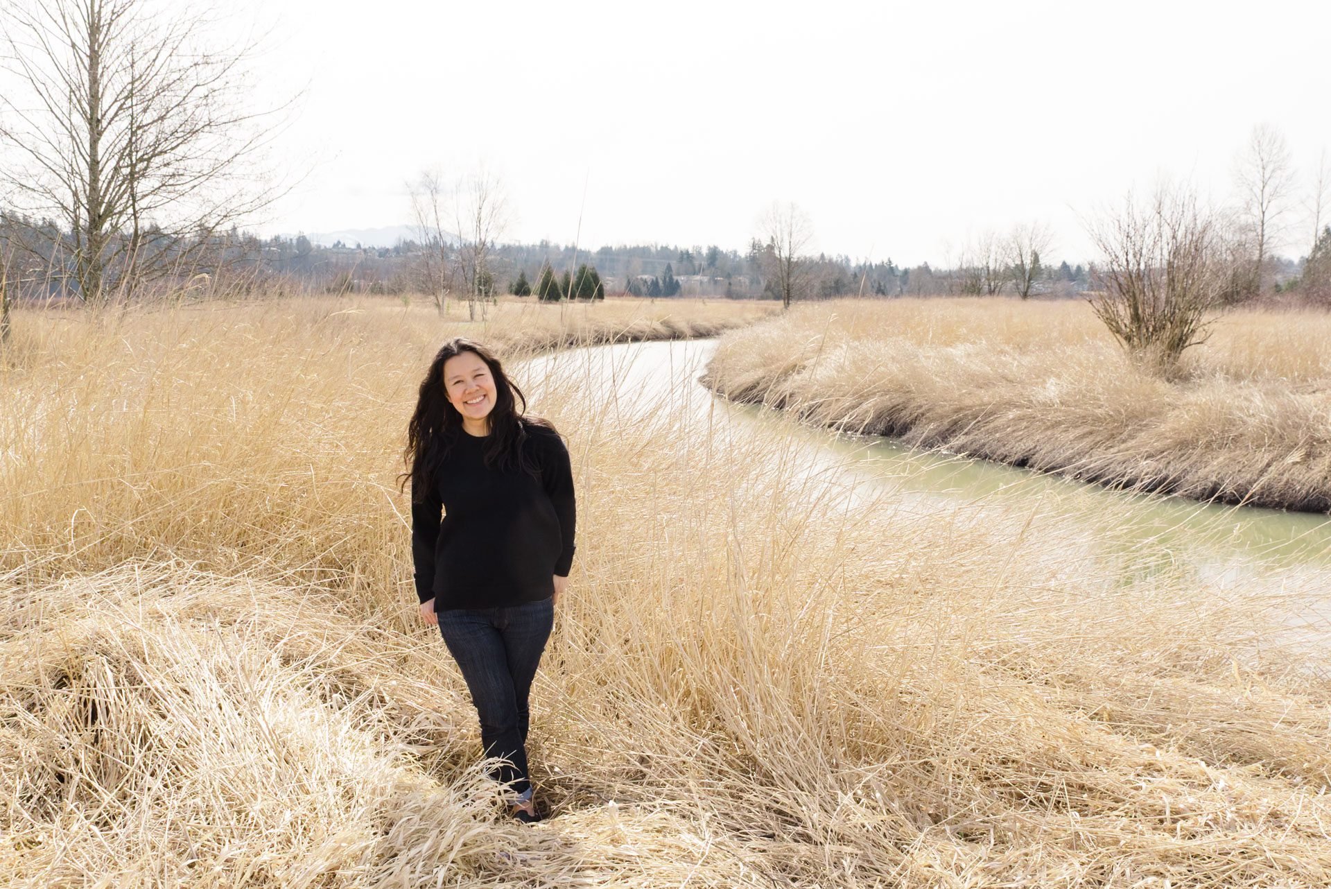 woman standing in a field of dry tall grass looking at the camera smiling
