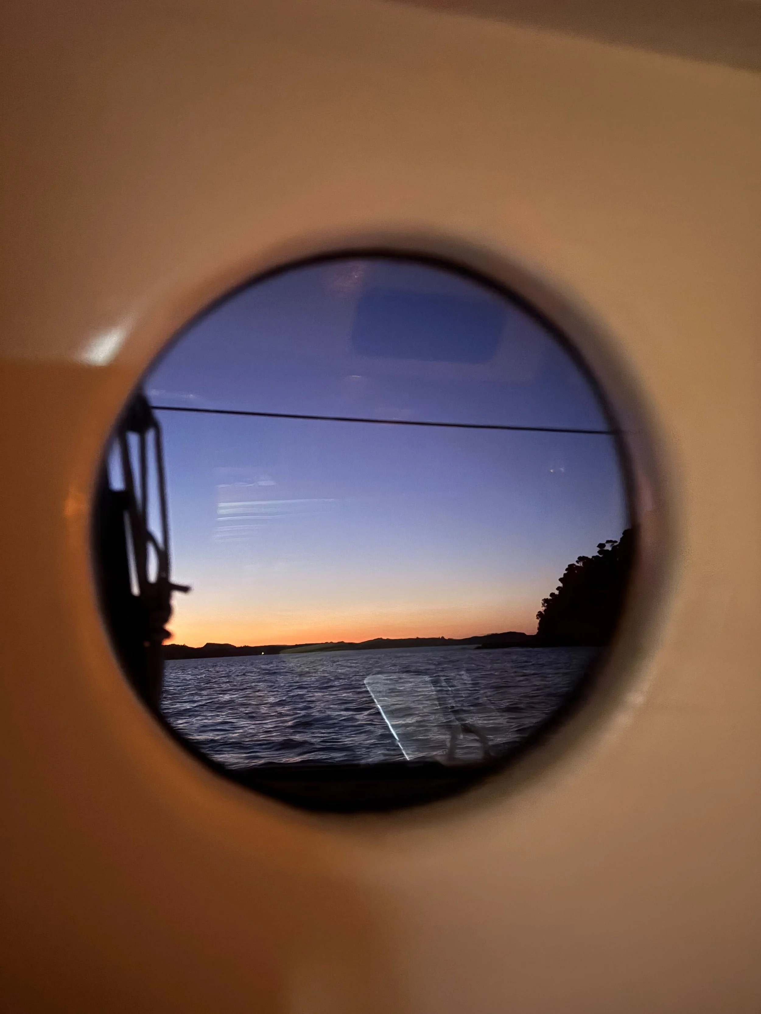 View of a sunset over water, seen through a circular porthole.