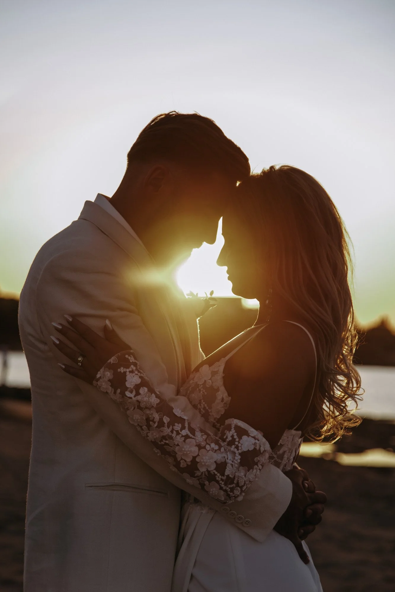 Couple embracing at sunset, their foreheads touching, on a beach.