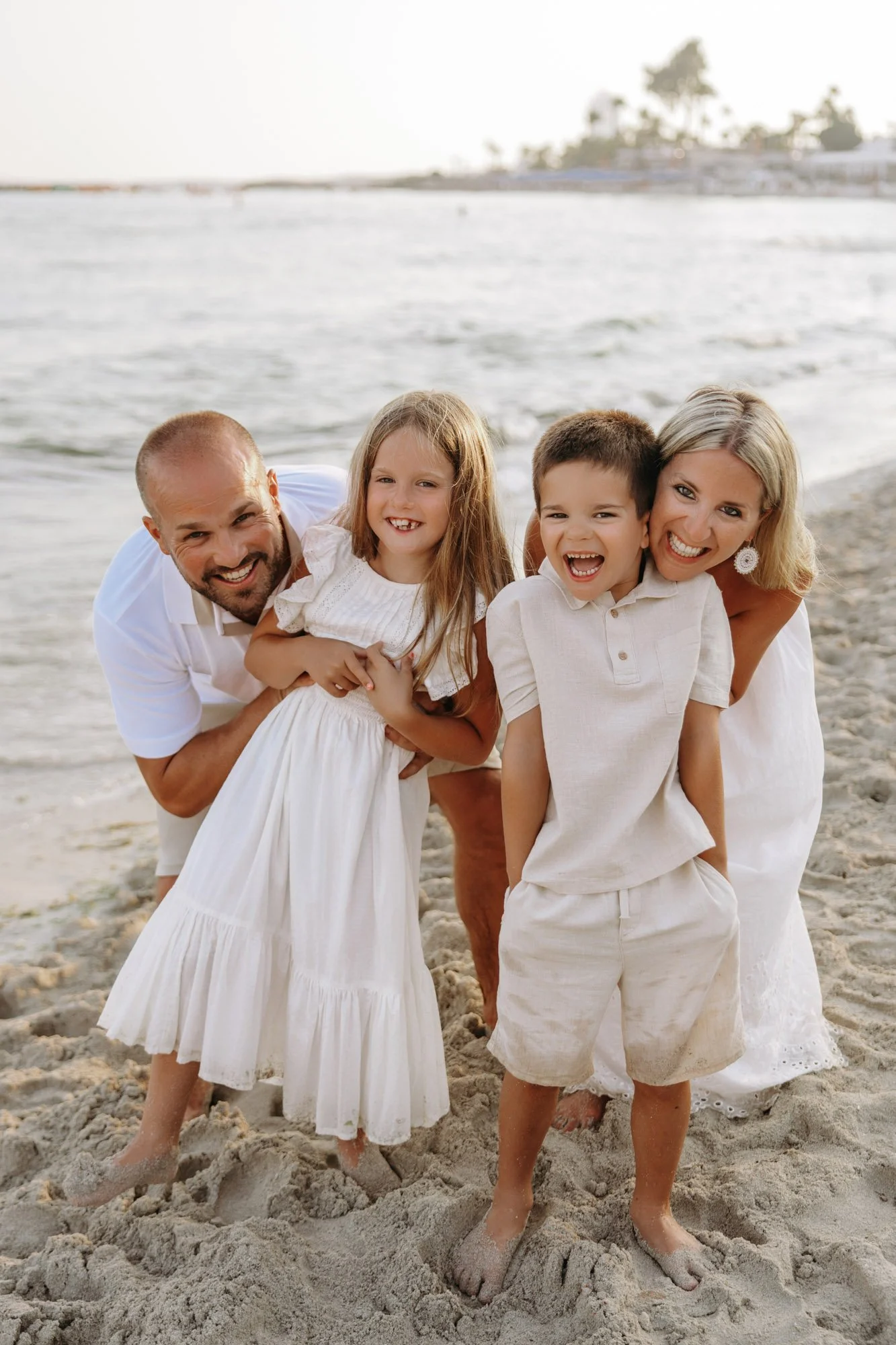 A happy family of four, consisting of a father, mother, and two children, enjoying time on the beach with sandy feet and smiling faces.