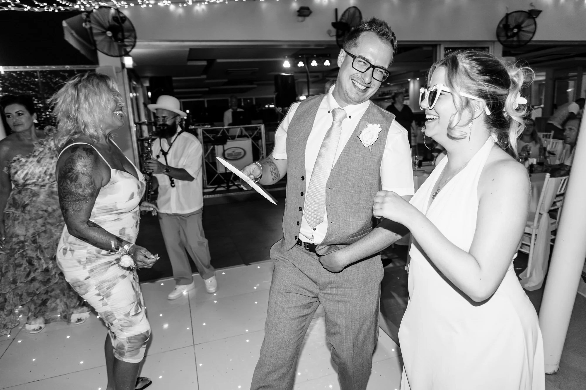 People dancing and celebrating at a wedding reception, including a couple in wedding attire and guests.