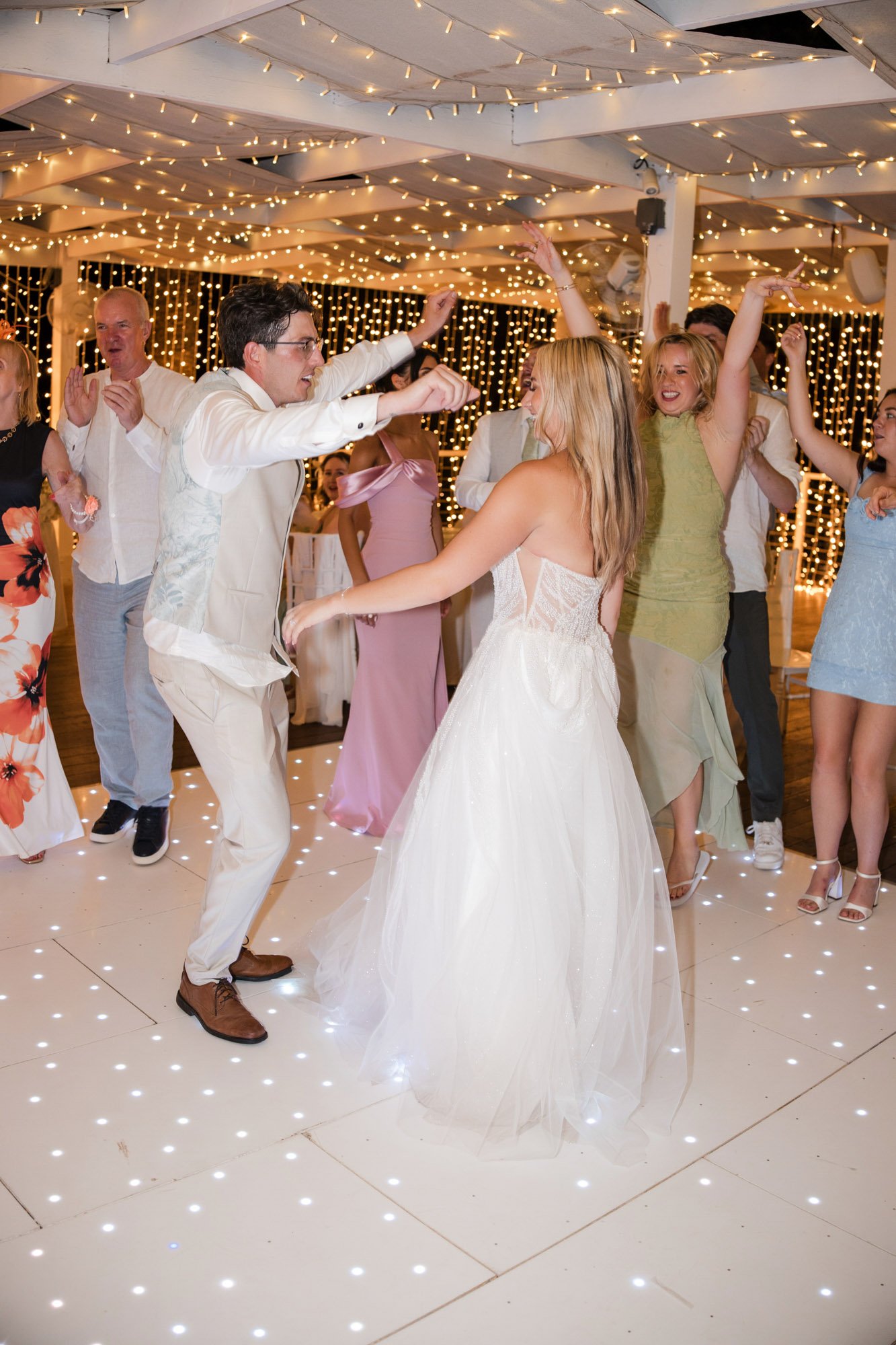 People dancing at a wedding reception with string lights in the background.