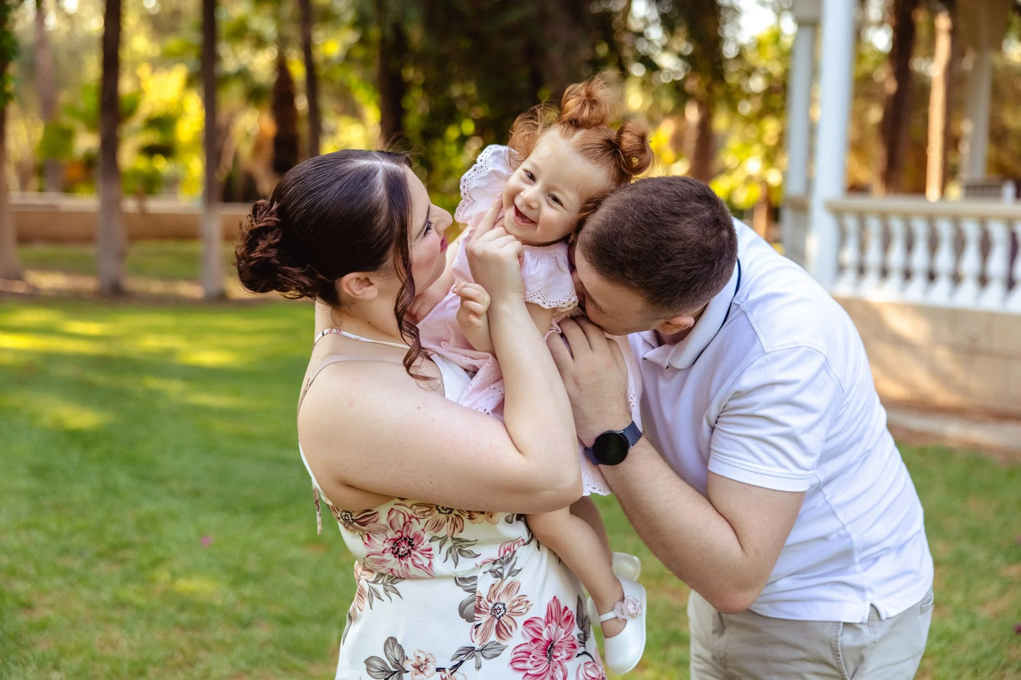 A family consisting of a mother, father, and young girl enjoying time together outdoors in a backyard or park on a sunny day.