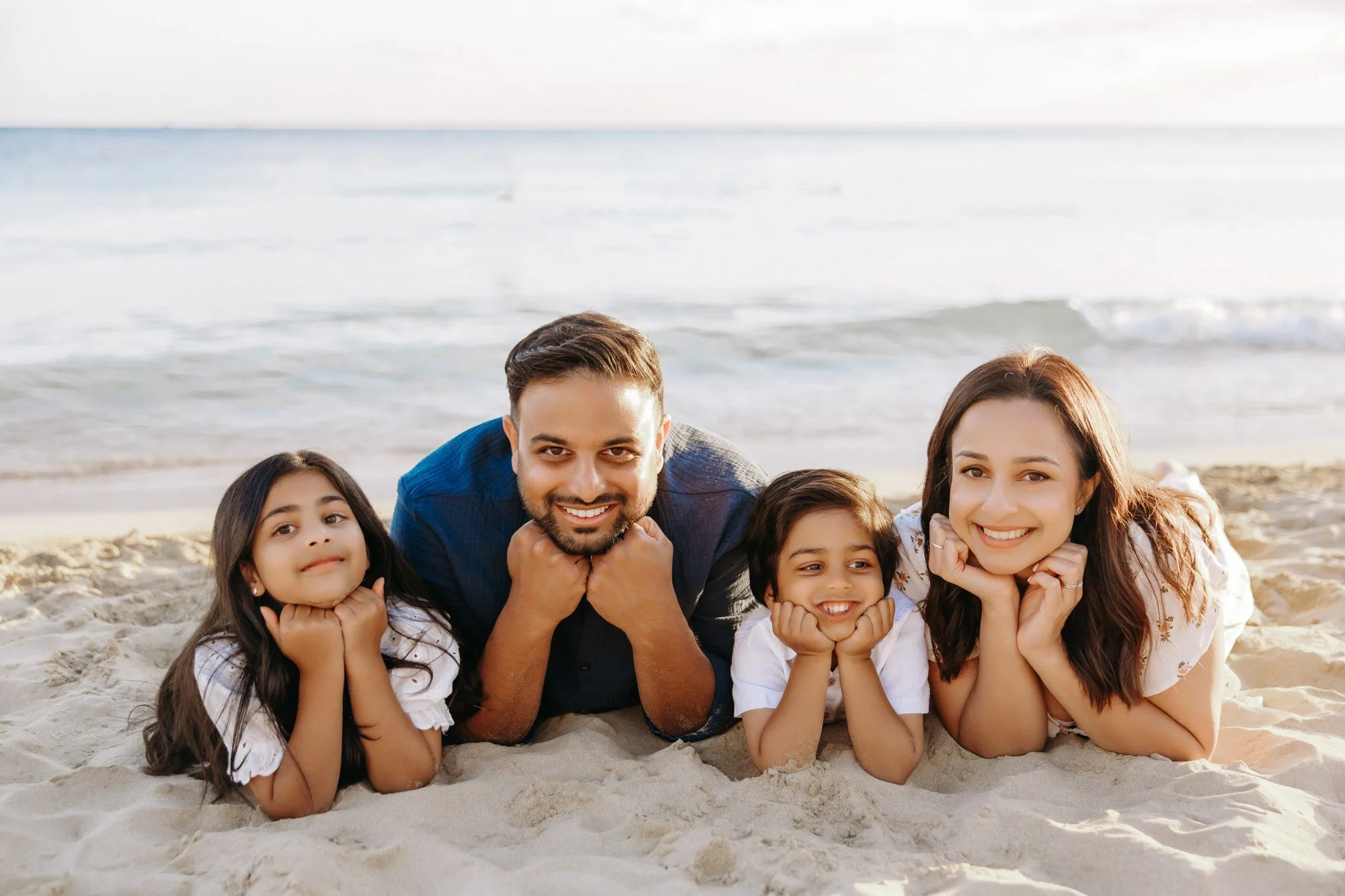 Family of five lying on the beach, smiling, with ocean waves in the background.