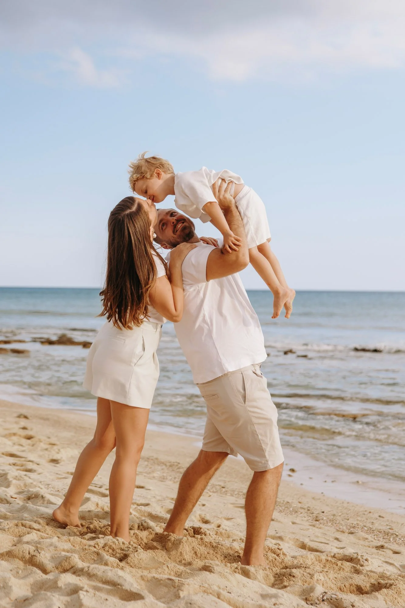 happy family photographer Ayia Napa lifting child by the sea during sunset session