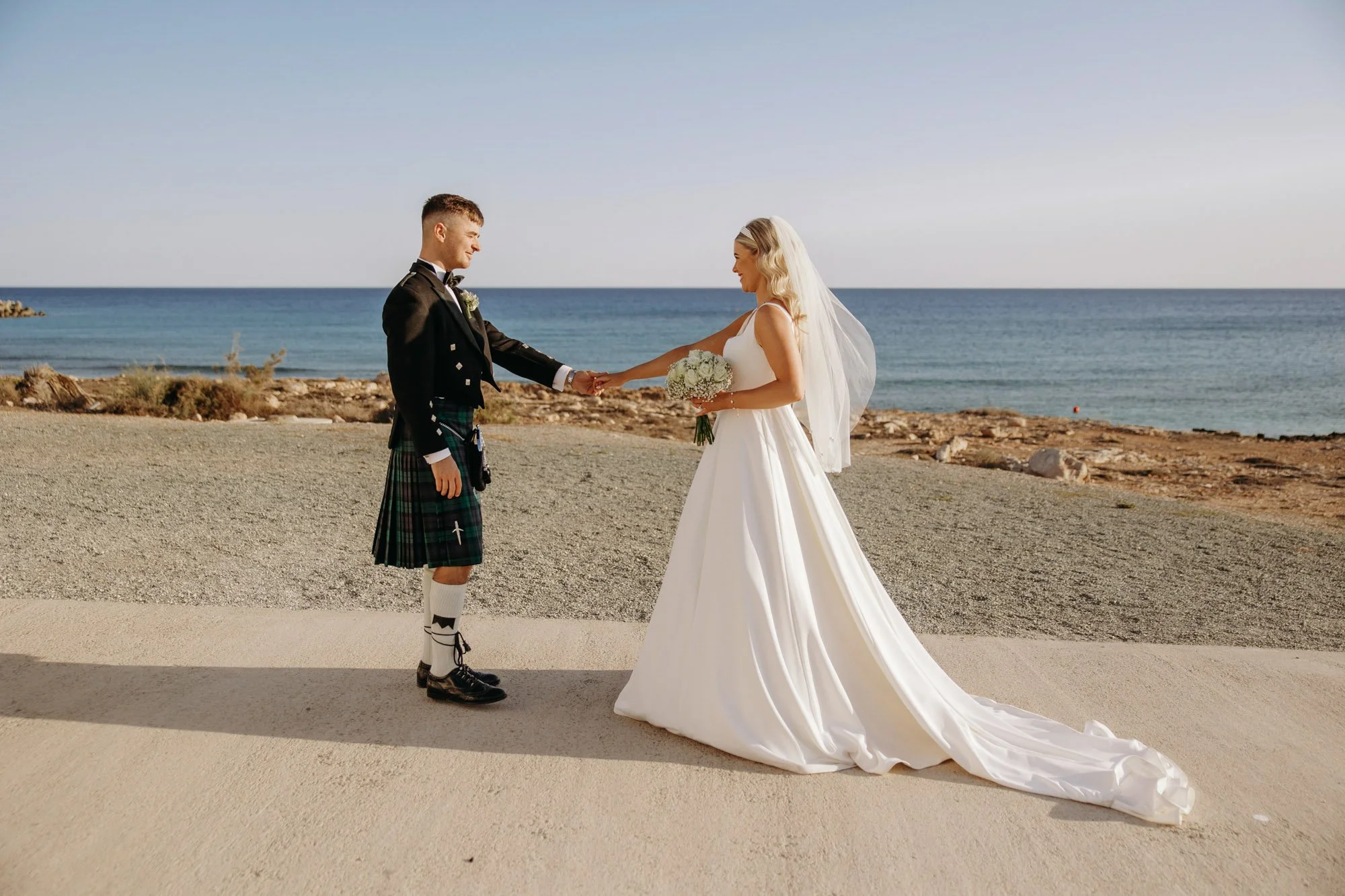 Bride and groom holding hands at their beach wedding, with ocean in the background.