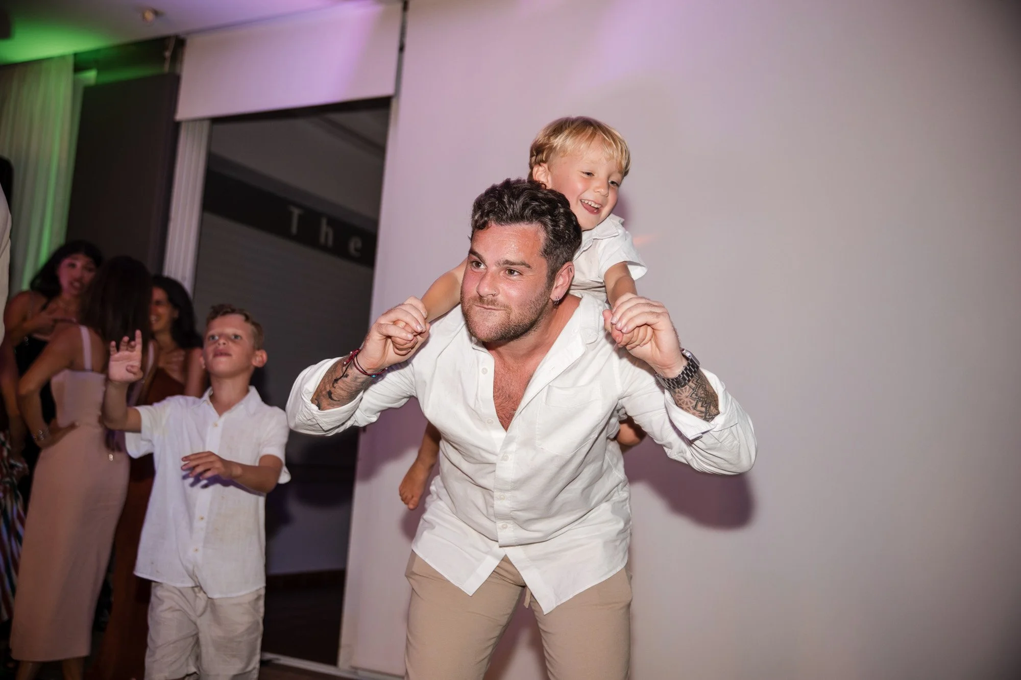 A man giving a piggyback ride to a young boy at a social event, with other people in the background.