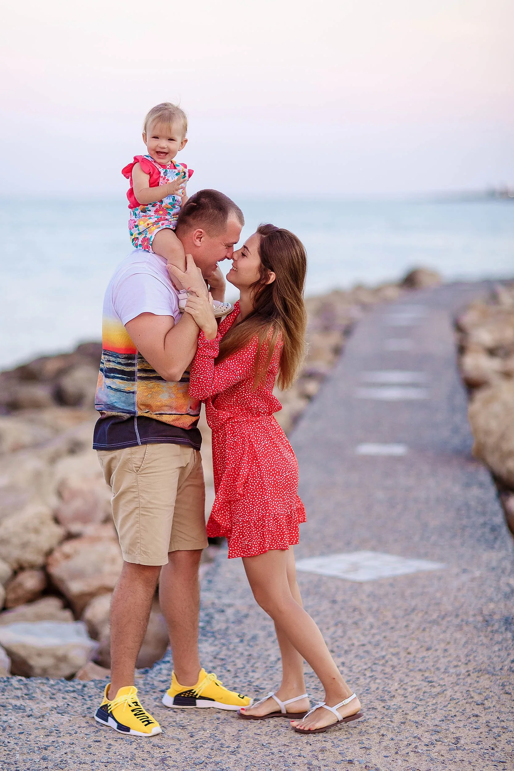 candid family moment Protaras beach walkway Cyprus parents holding baby sunset light
