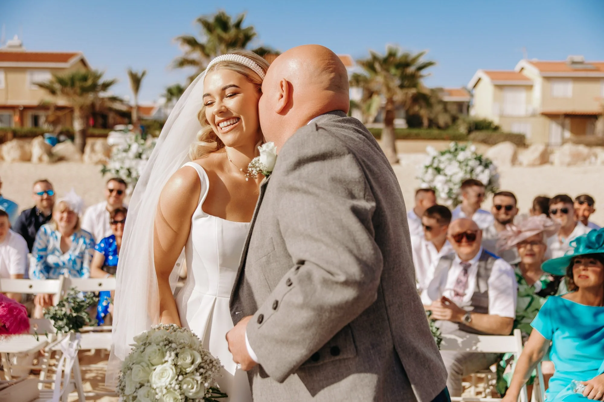 A bride and man share a moment at an outdoor wedding ceremony, with guests seated behind them.