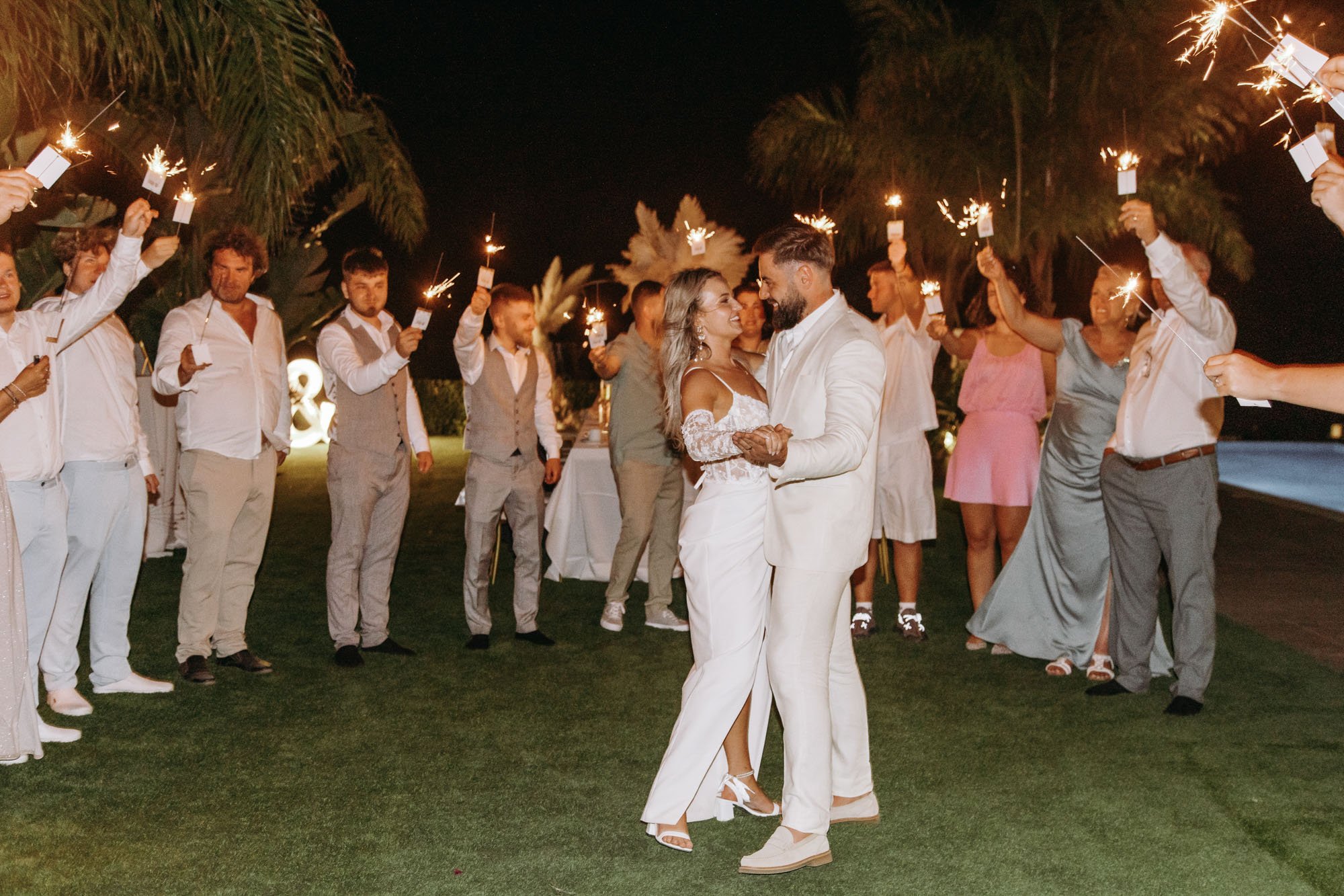 A bride and groom dance together surrounded by guests holding sparklers at night during a wedding celebration.