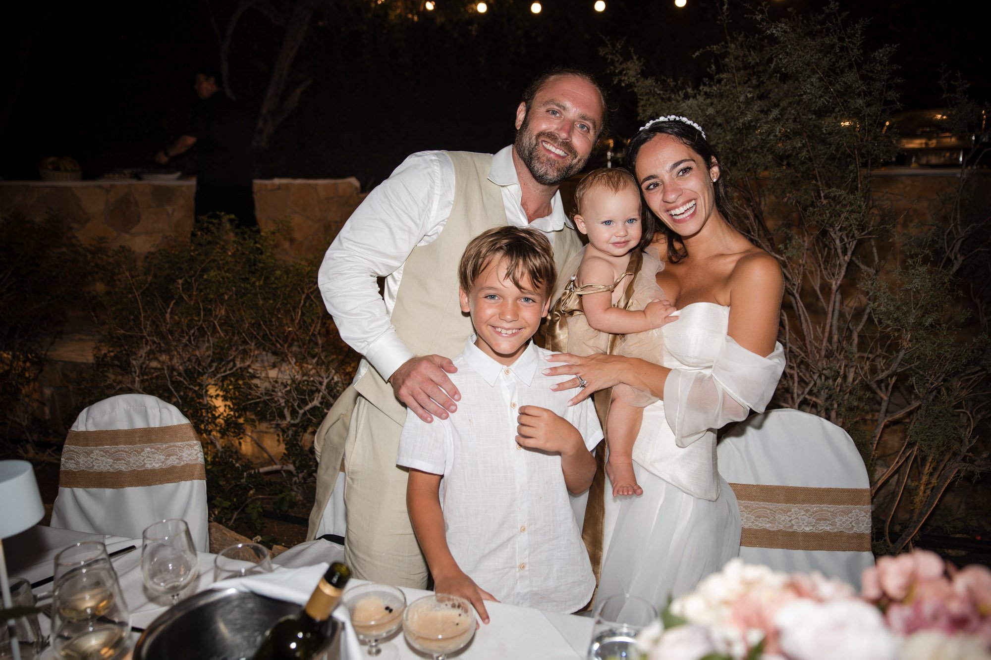 A happy family celebrating at a dinner table during a special occasion, with a man, woman, and two children smiling for the camera, outdoors at night.