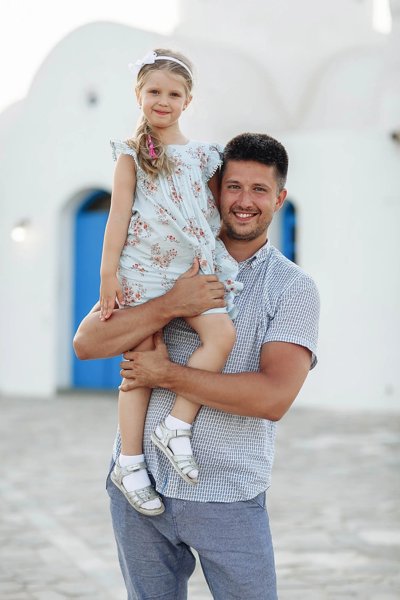 A man holding a young girl in his arms in front of white buildings with blue doors.