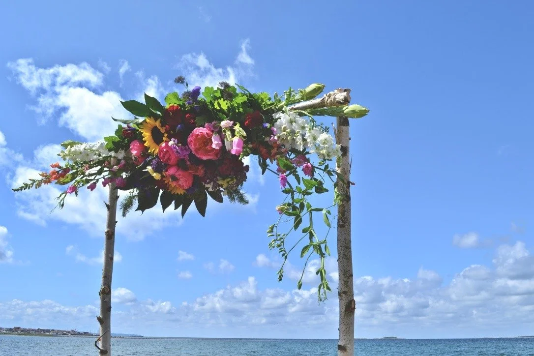 Färgglad blomsterdekoration på en träställning med hav och blå himmel i bakgrunden.