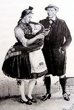 This black-and-white illustration or early photograph depicts a couple in traditional European clothing, with the mother carrying a baby in a cloth sling on her front. Her attire — including a full, pleated skirt, apron, and detailed bodice — suggest