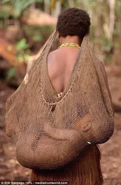 This extraordinary image shows a mother from Papua New Guinea carrying her baby in a traditional bilum, a hand-woven string bag made from plant fibers. Worn across the shoulders or forehead, the bilum gently cradles the baby against her back, allowin