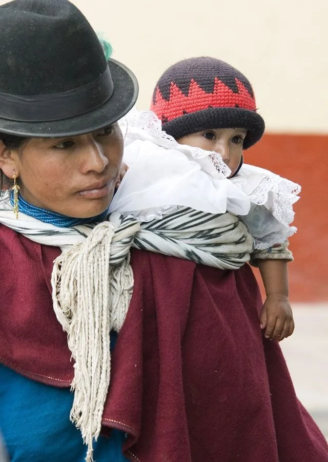 Wrapped close in a thick, striped rebozo, the baby rides high on their mother’s back, cradled against the soft wool folds of her shawl. A handwoven knot secures the cloth at her chest, timeworn and sure in its strength. The woman’s traditional felt h