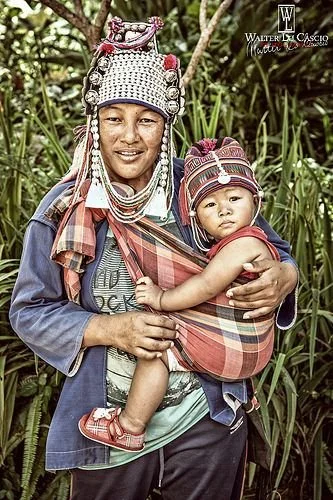 This vibrant photograph shows a woman from the Akha ethnic group, one of the Indigenous hill tribes of Southeast Asia, particularly found in northern Thailand, Laos, Myanmar, and southern China. She wears the distinctive Akha headdress adorned with s