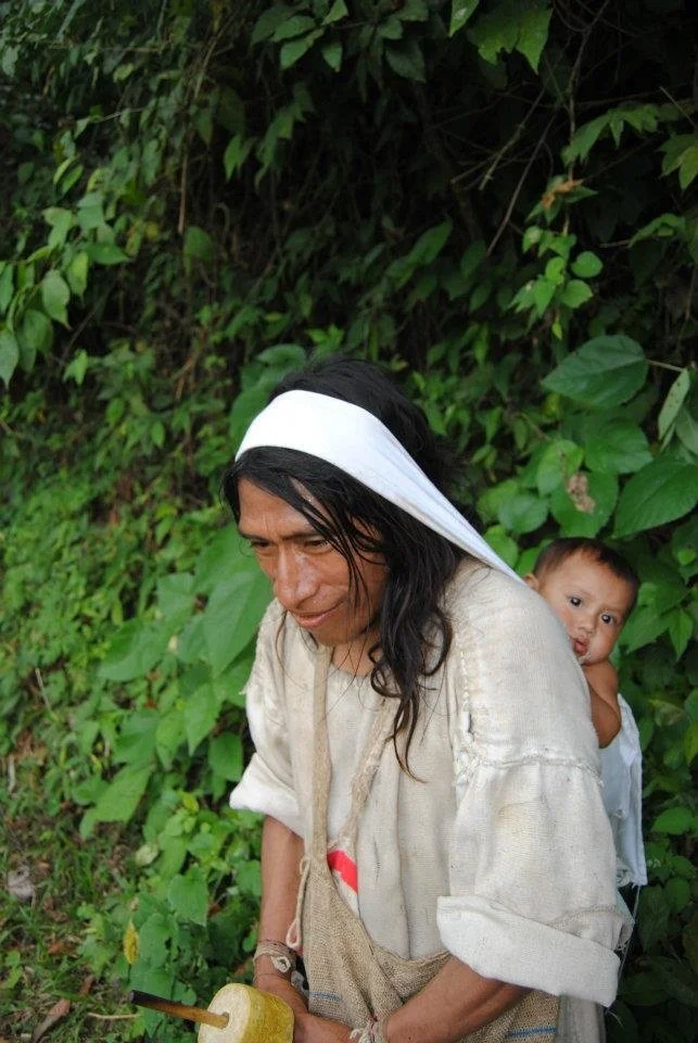 A father carries his child with quiet strength and presence, nestled against his back in a soft cloth sling. This image, captured in the lush green foothills of Colombia’s Sierra Nevada de Santa Marta, reflects the enduring caregiving roles held by K