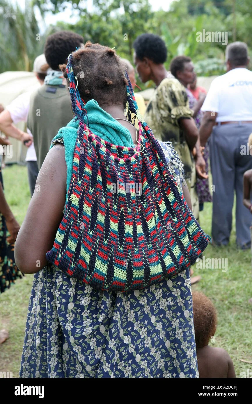 In this vibrant image, a Tolai woman from East New Britain, Papua New Guinea, carries her baby in a woven bag known locally as a bilum. The bilum, made from strong, hand-twisted fiber or yarn, is carried from the head, allowing the bag to hang agains