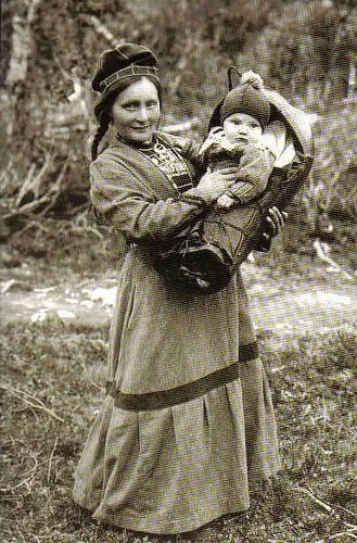 Among the Sámi people of the far north, babies are carried in beautifully crafted cradleboards called komse, wrapped in furs and love against the Arctic winds. Here, a mother holds her child nestled in a komse, her traditional dress echoing the fores