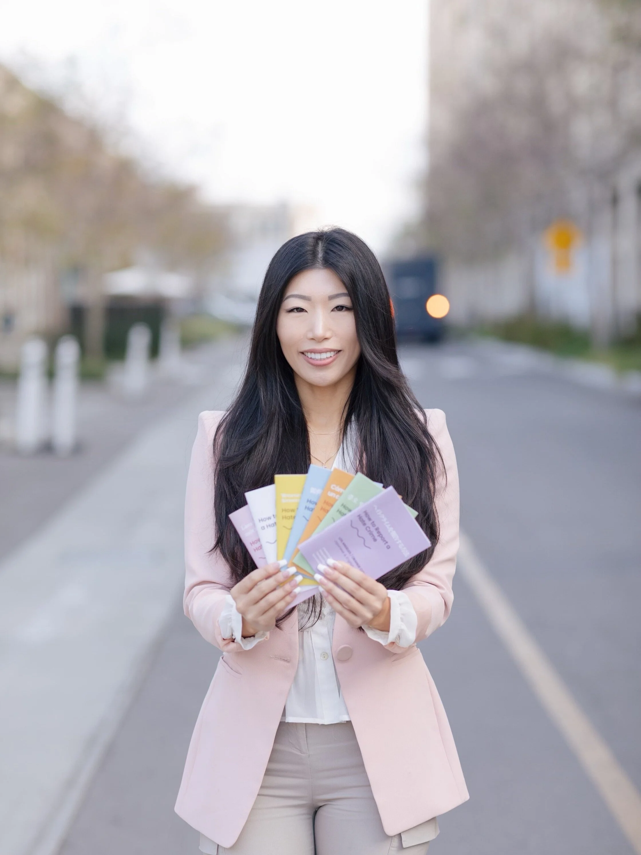 Esther in a pink blazer holding colorful pamphlets, standing on a city street with blurred background.