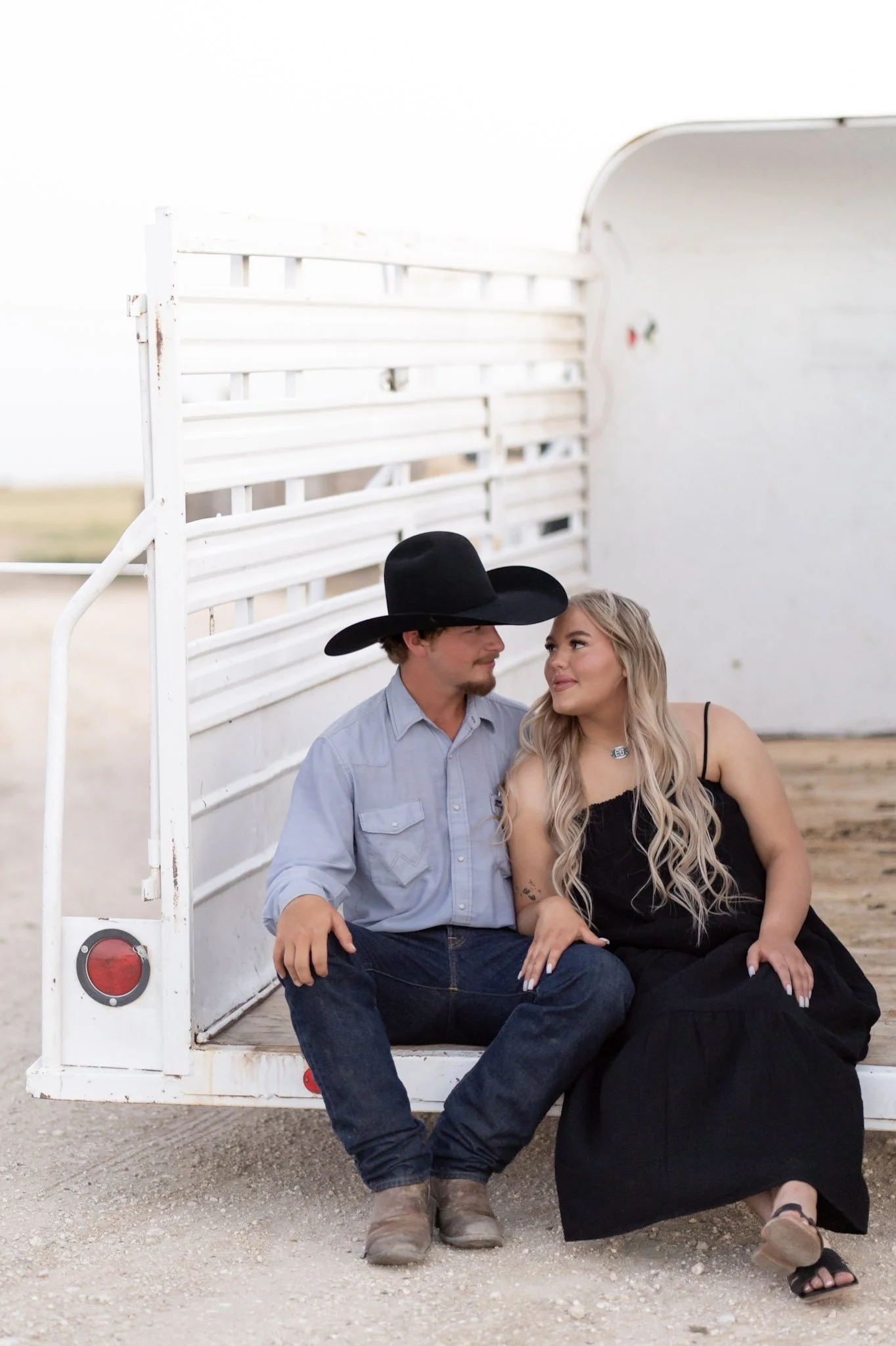 A smiling couple in a western settling, sitting on a horse trailer smiling