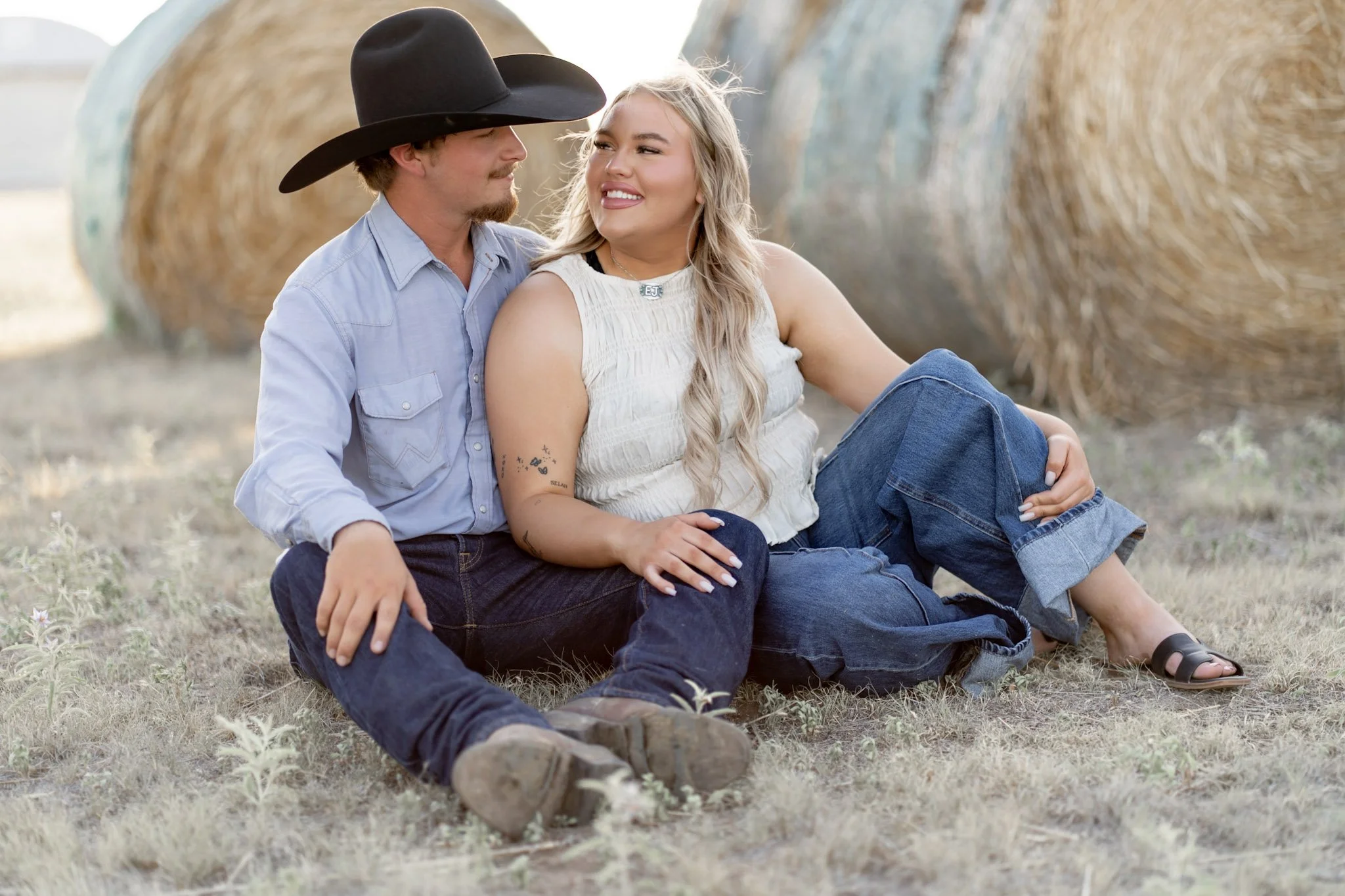 a texas couple sitting in front of some hay bales on the farm