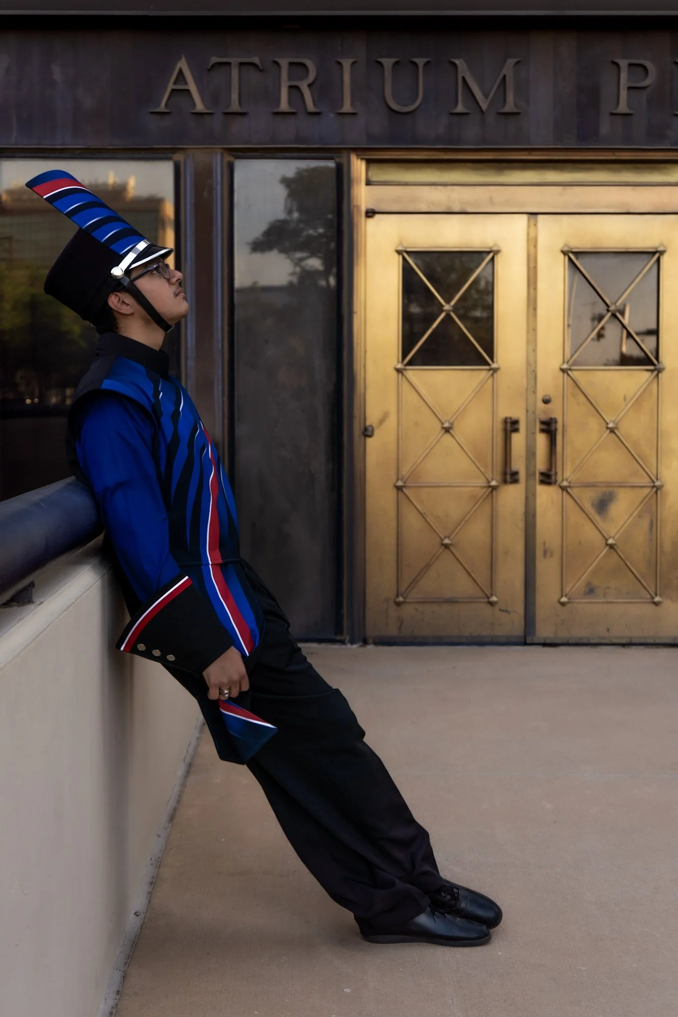 Person dressed in a band uniform leaning against a wall with a gold-colored double door behind them.
