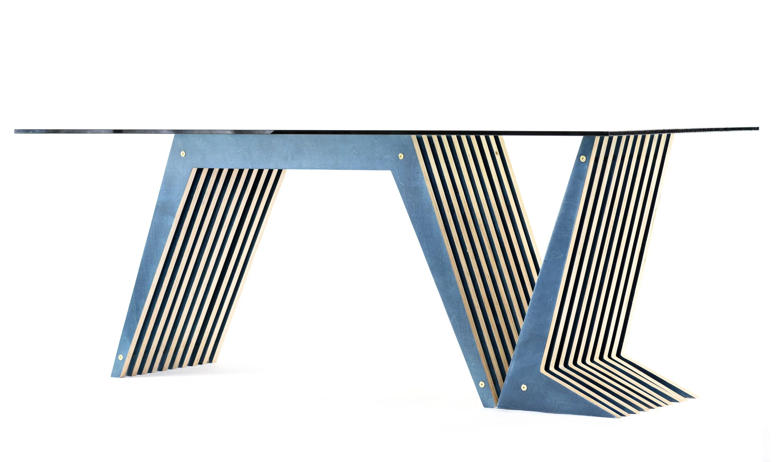 Modern architectural desk with geometric angular blue finish base and a flat tempered glass top, featuring layered unique shape slatted wooden legs, set against a white background.