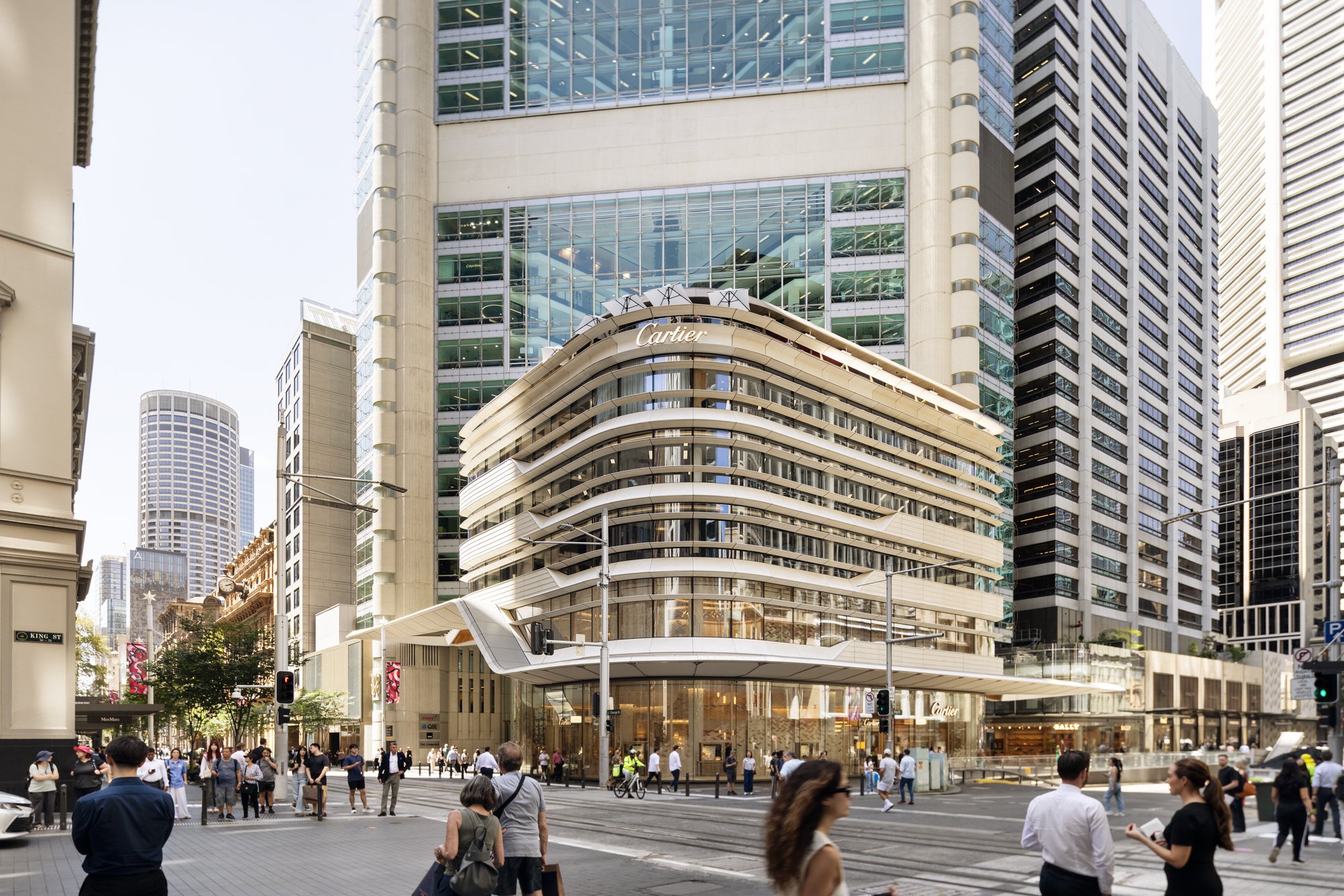 A busy city street scene with people crossing the road in front of a modern, multi-story Cartier building in a financial district. Designed by fjcStudio Photo by Ruth Gold