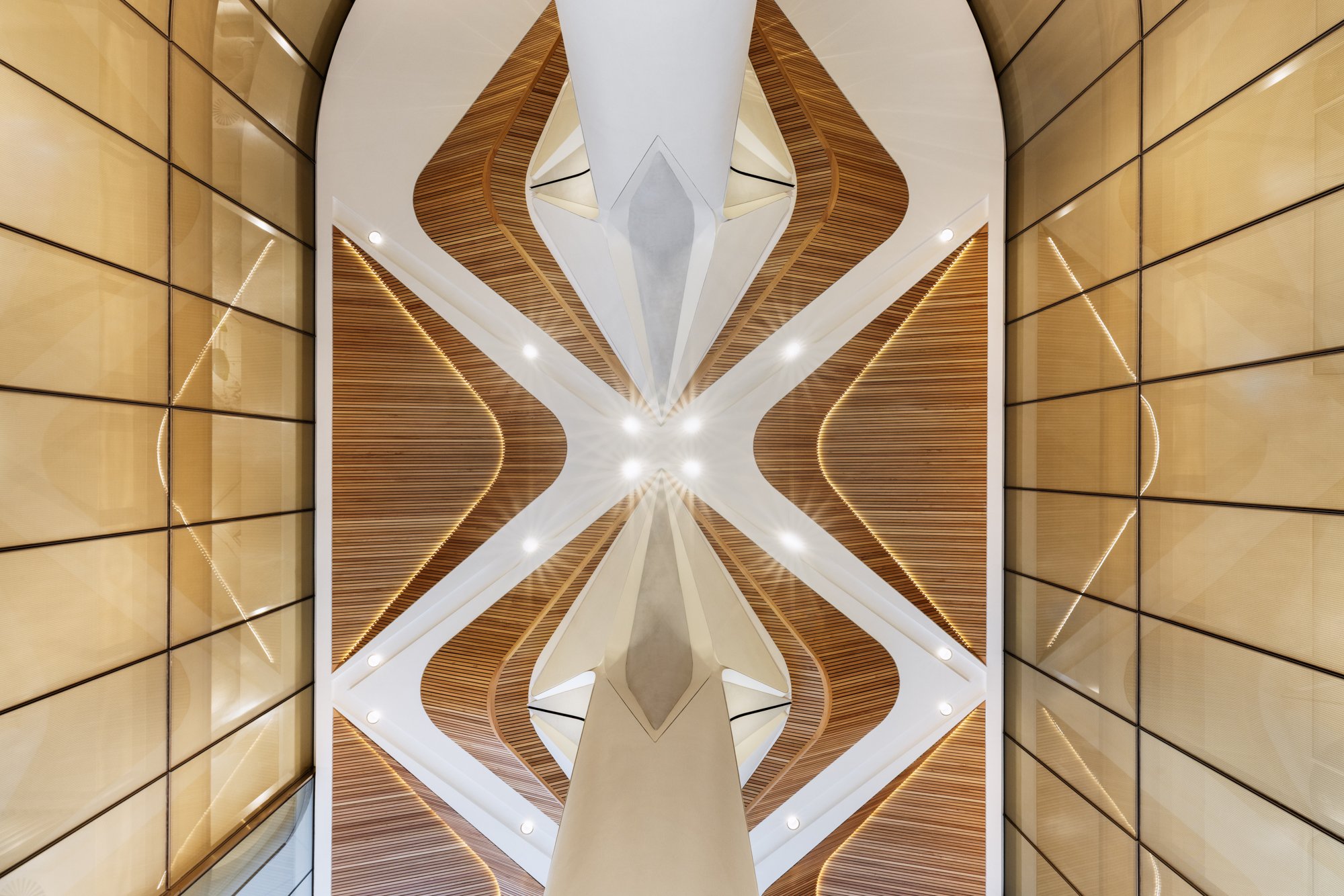 Interior ceiling view of a modern building with geometric design, wooden and white elements, lighting, and mirrors. Designed by fjcStudio Photo by Ruth Gold