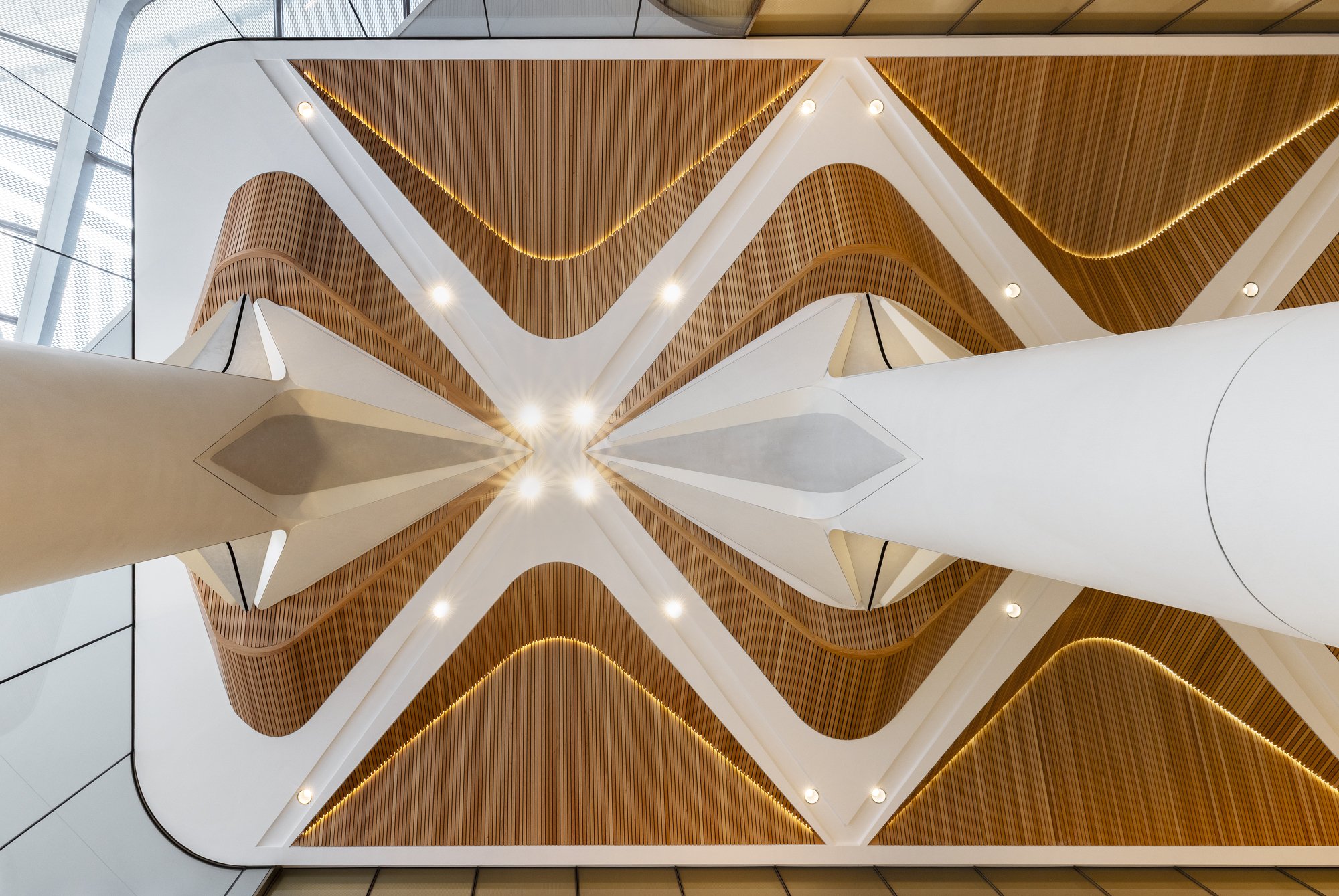 Interior view of a modern building with architectural ceiling design featuring wood panels, white structural elements, and lighting fixtures. Designed by fjcStudio Photo by Ruth Gold