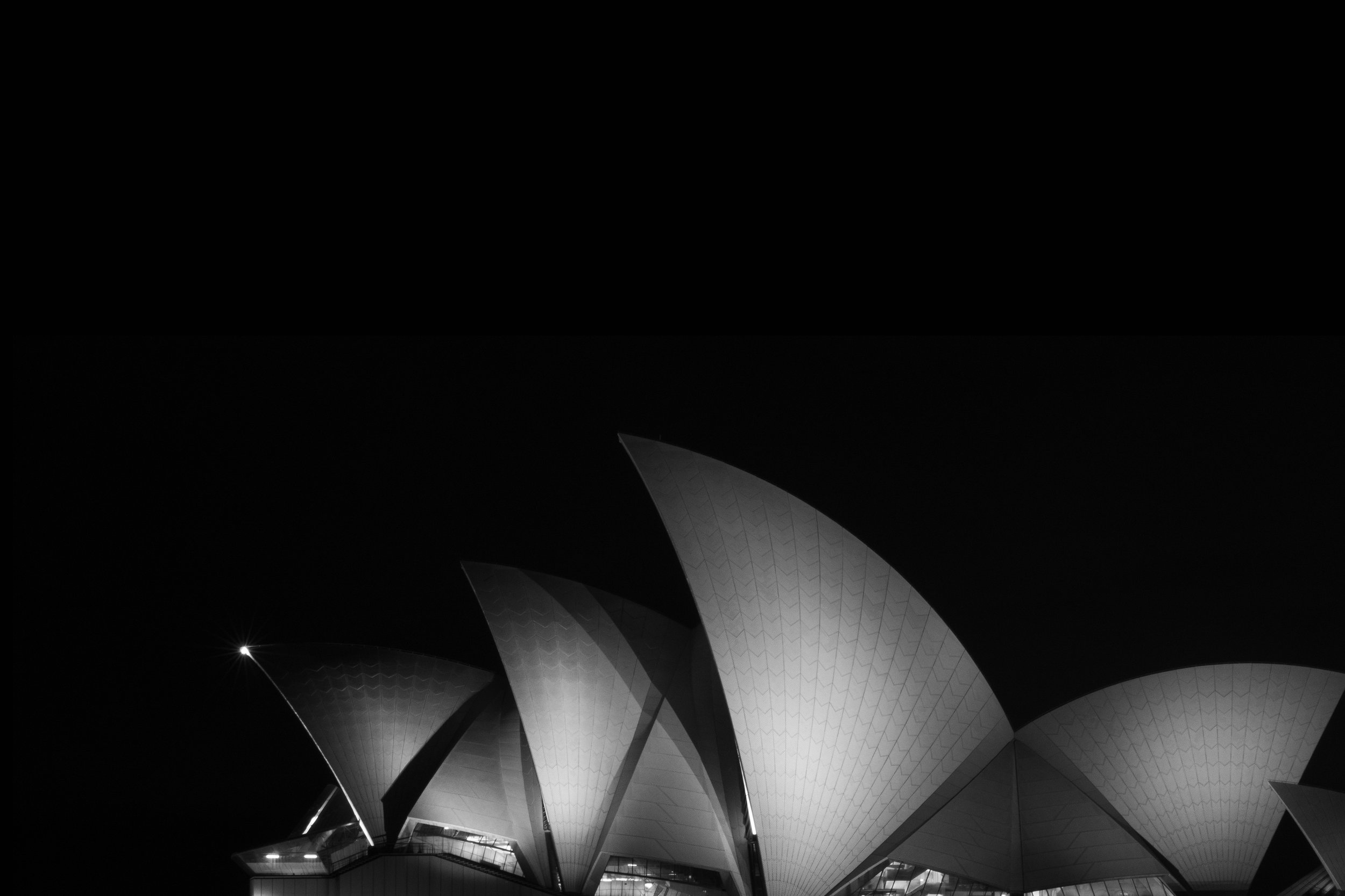 Night view of the Sydney Opera House with its iconic sail-shaped roof structures illuminated against the dark sky. Opera House Photo by Ruth Gold