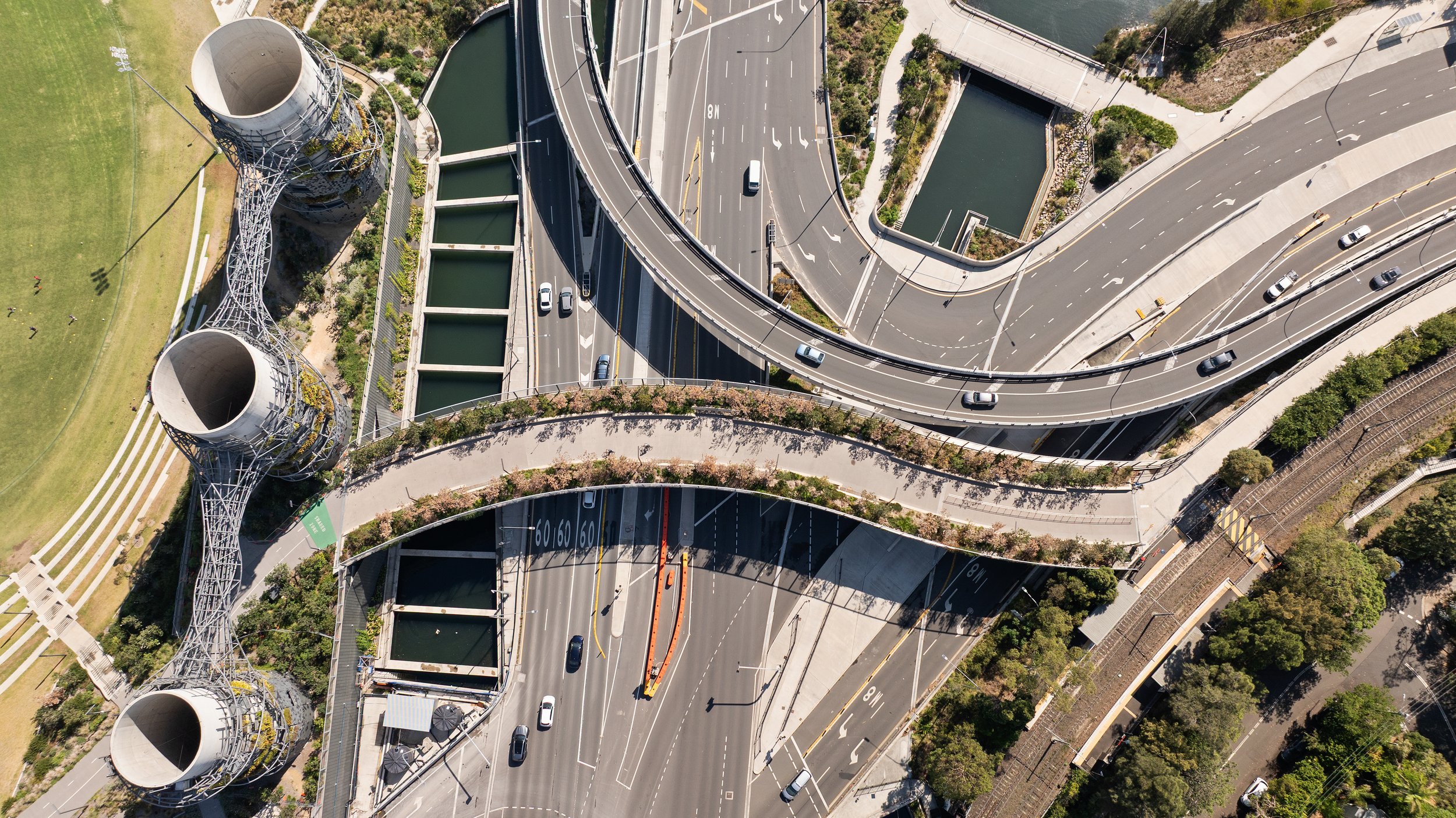 Aerial view of a multi-level highway interchange with cars, roads, greenery, and large industrial structures. Designed by McGregor Coxall Photo by Ruth Gold