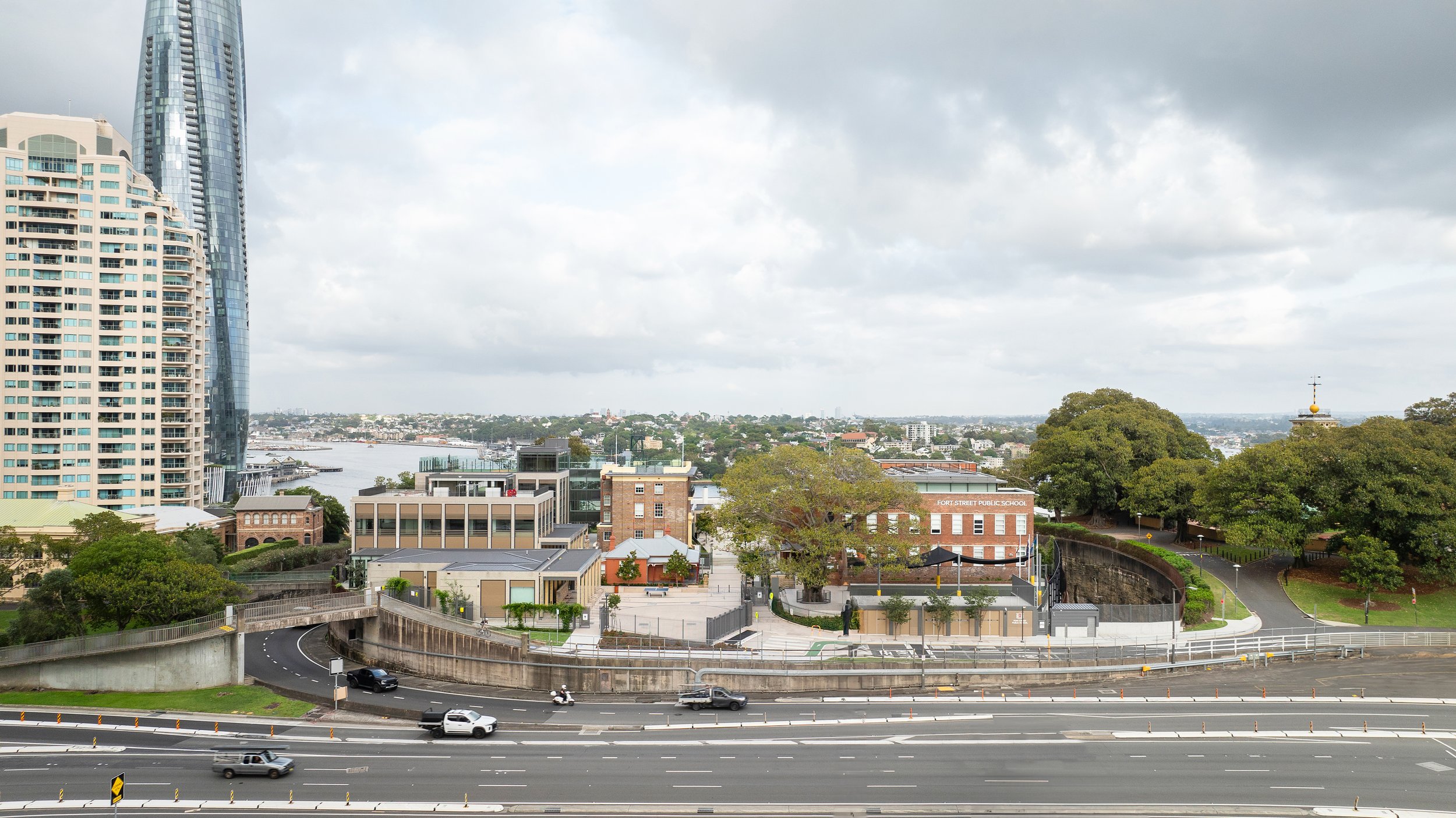 Cityscape view showing high-rise buildings, a river in the background, and a road with cars in the foreground. Designed by fjcStudio Photo by Ruth Gold