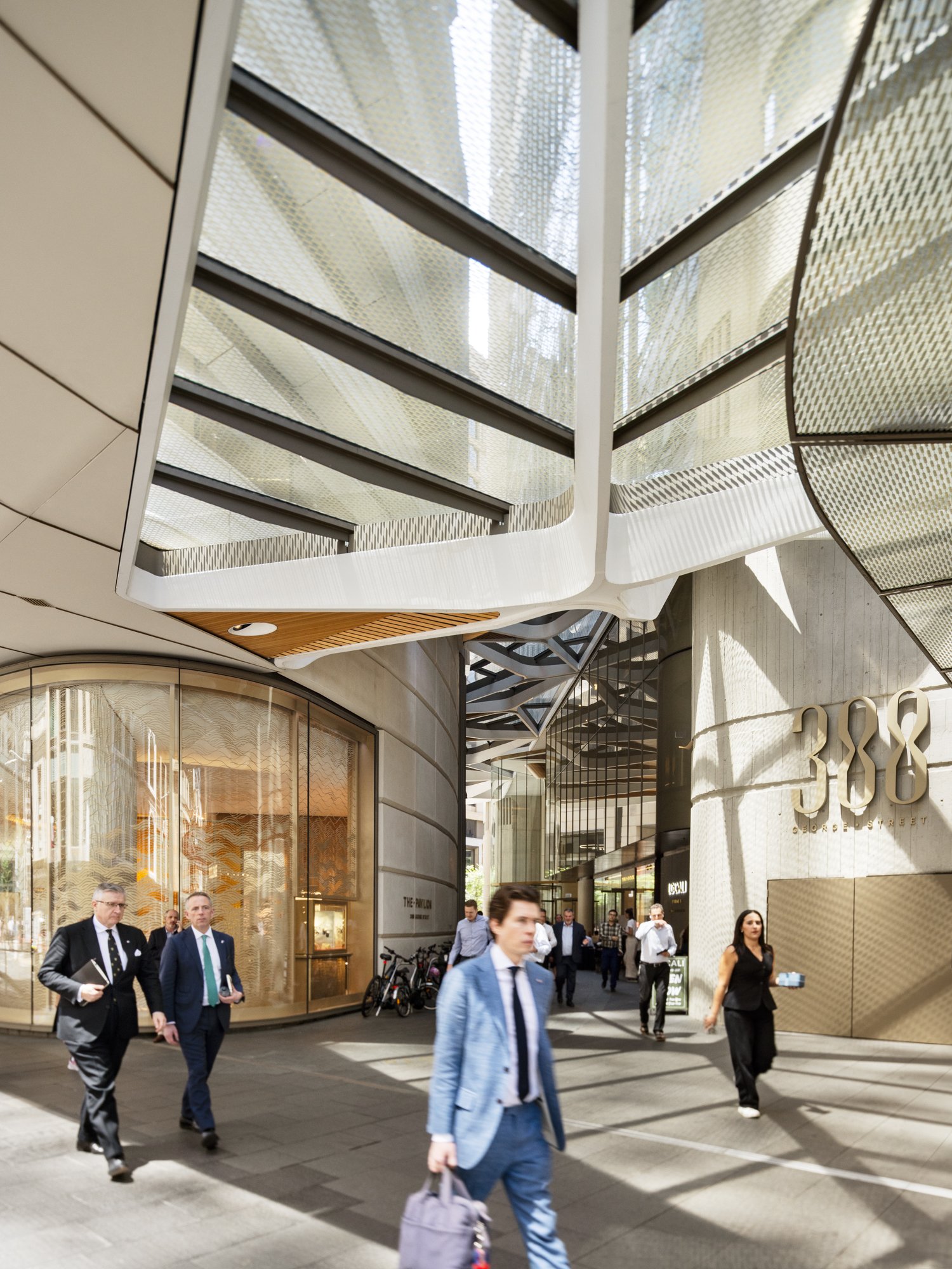 People walking outside a modern building with large glass windows and unique architectural features. Designed by fjcStudio Photo by Ruth Gold