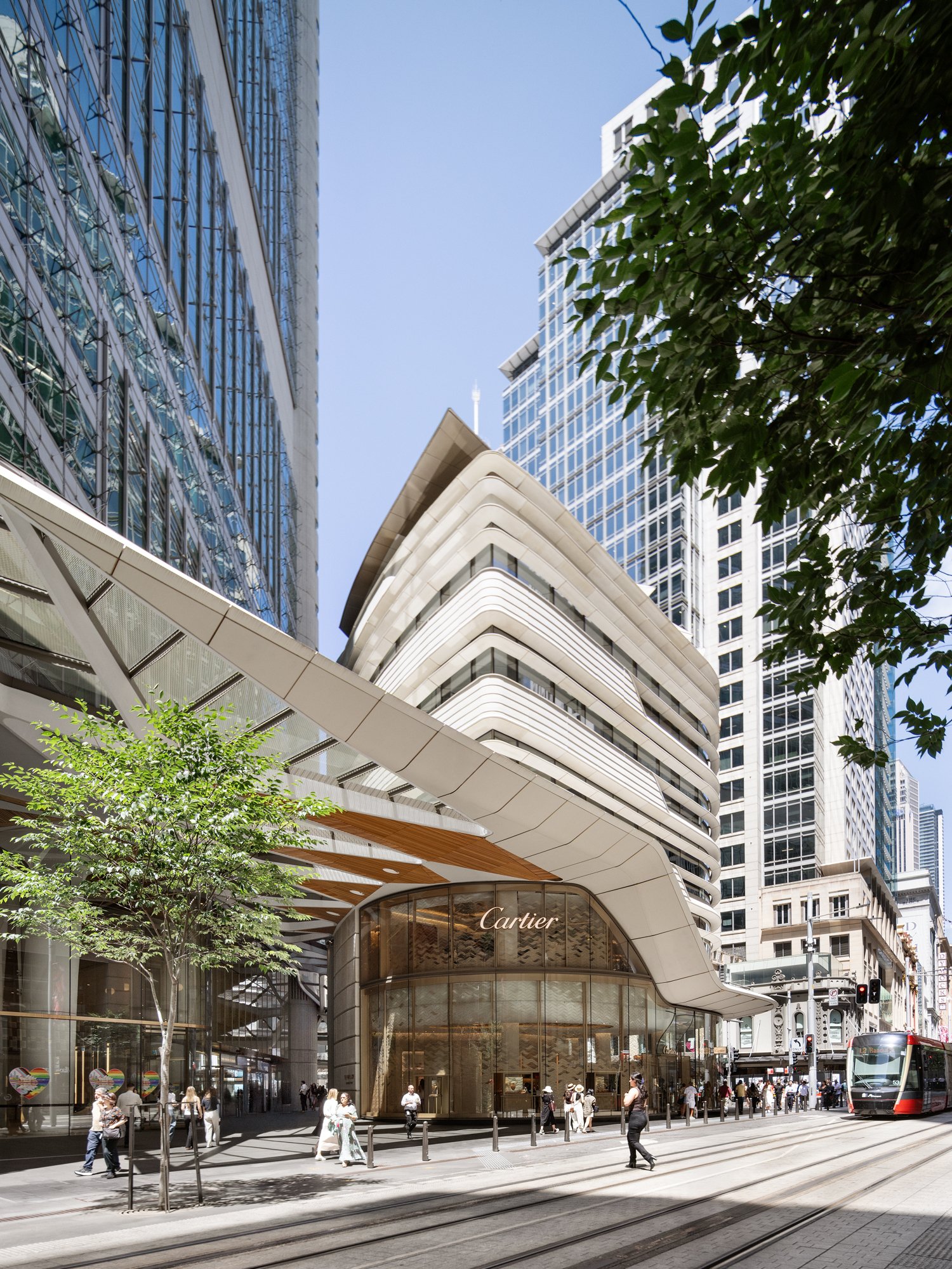 City street scene with modern buildings, a Cartier store with glass facade, pedestrians walking, and a tram on the tracks. Designed by fjcStudio Photo by Ruth Gold