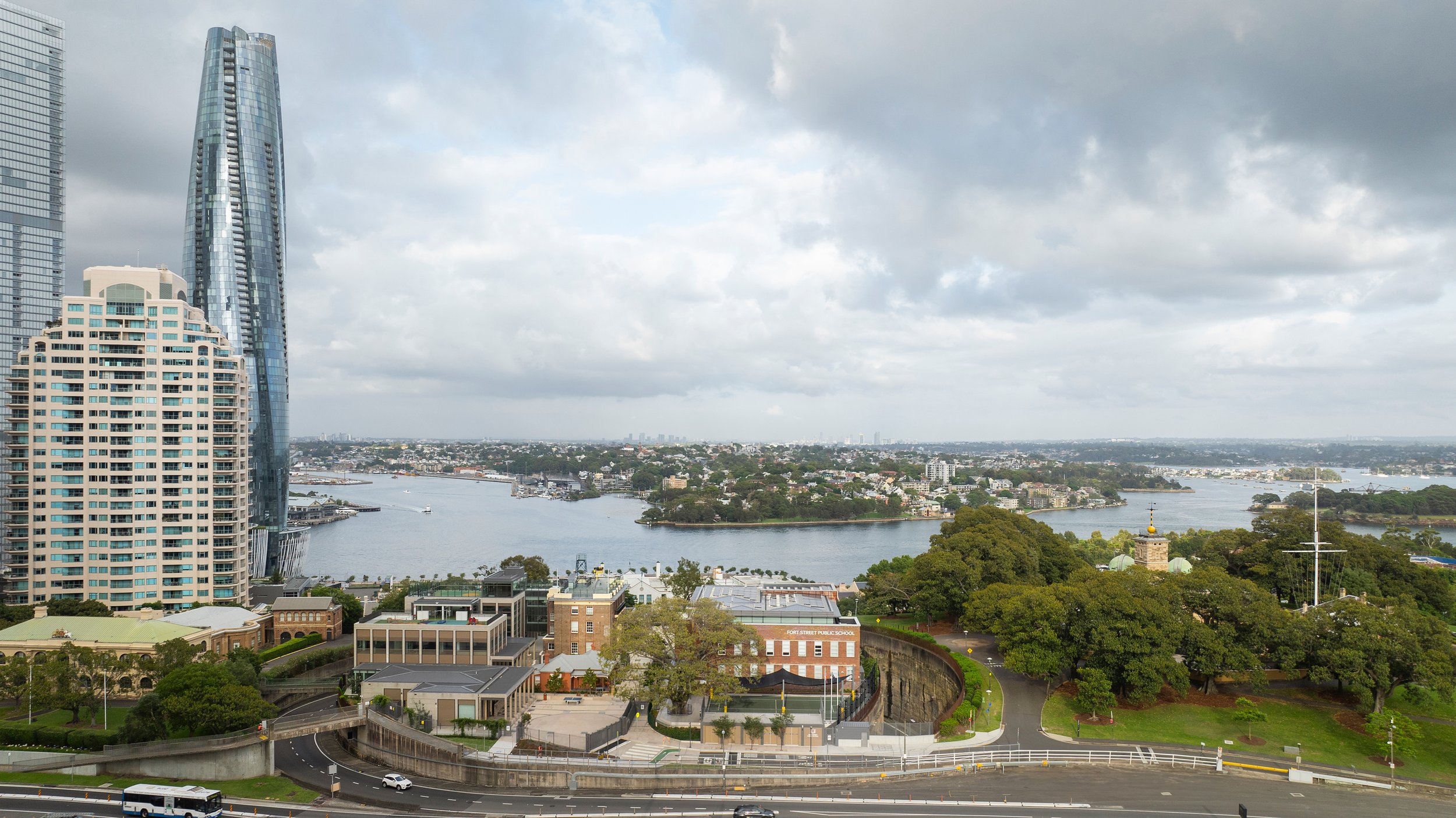 City skyline with tall modern skyscrapers, a river, green parks, and a cloudy sky. Designed by fjcStudio Photo by Ruth Gold