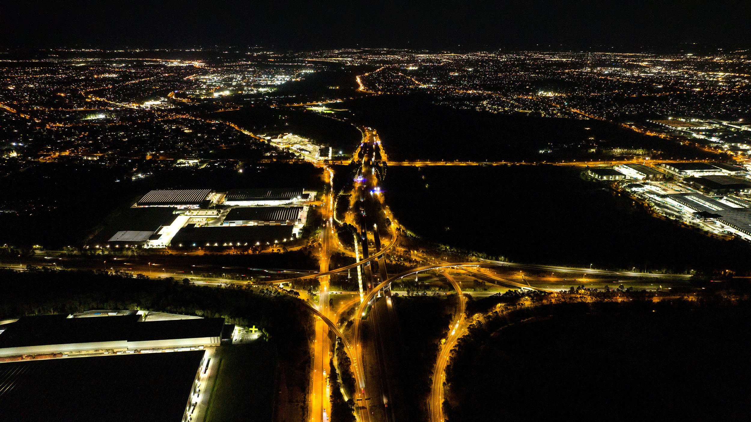 Aerial night view of a city with illuminated roads and buildings, and a dark park area in the center. Designed by Colin Polwarth Studio Photo by Ruth Gold