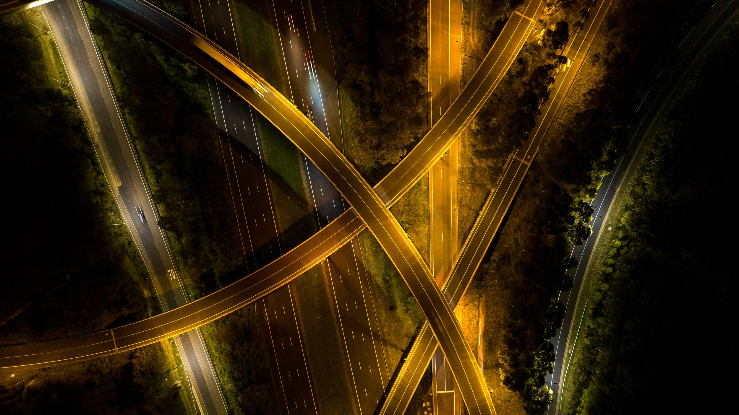 Aerial night view of an illuminated highway interchange with multiple overpasses crossing each other. Designed by Colin Polwarth Studio Photo by Ruth Gold