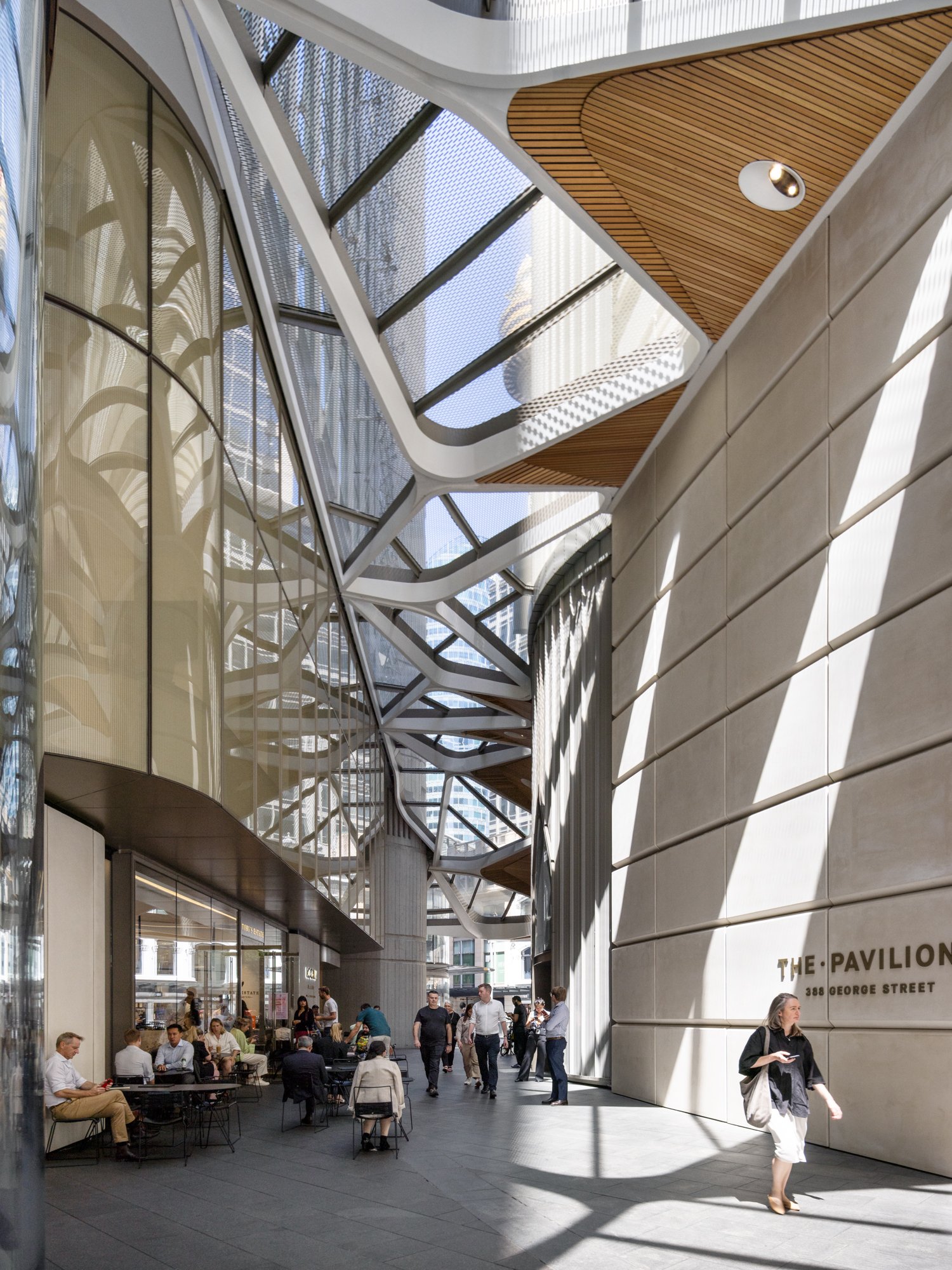 Indoor area with modern architectural design, large glass ceiling, and people sitting and walking around. Designed by fjcStudio Photo by Ruth Gold