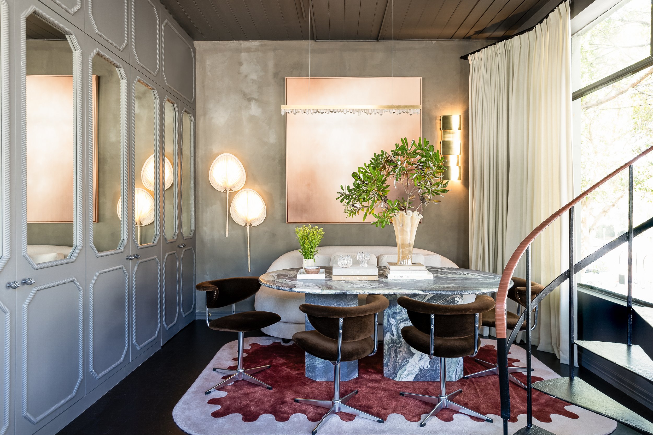 Stylish dining room with a marble table, brown velvet chairs, decorative lighting, large window with curtains, and modern decor. SMAC Studio Photo by Ruth Gold.