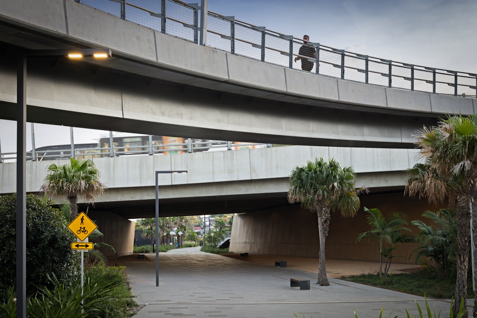 A pedestrian and bicycle path underneath a multi-level concrete highway overpass. Designed by Colin Polwarth Studio Photo by Ruth Gold
