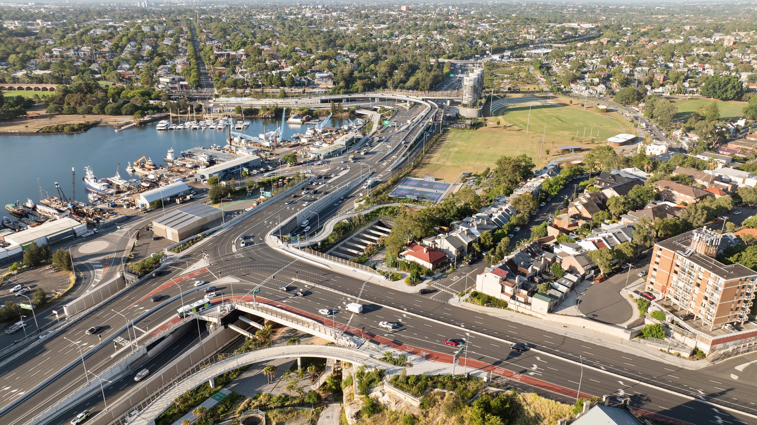 An aerial view of a city showing roads, a marina with boats, residential houses, apartments, a park, and athletic courts. Designed by McGregor Coxall Photo by Ruth Gold