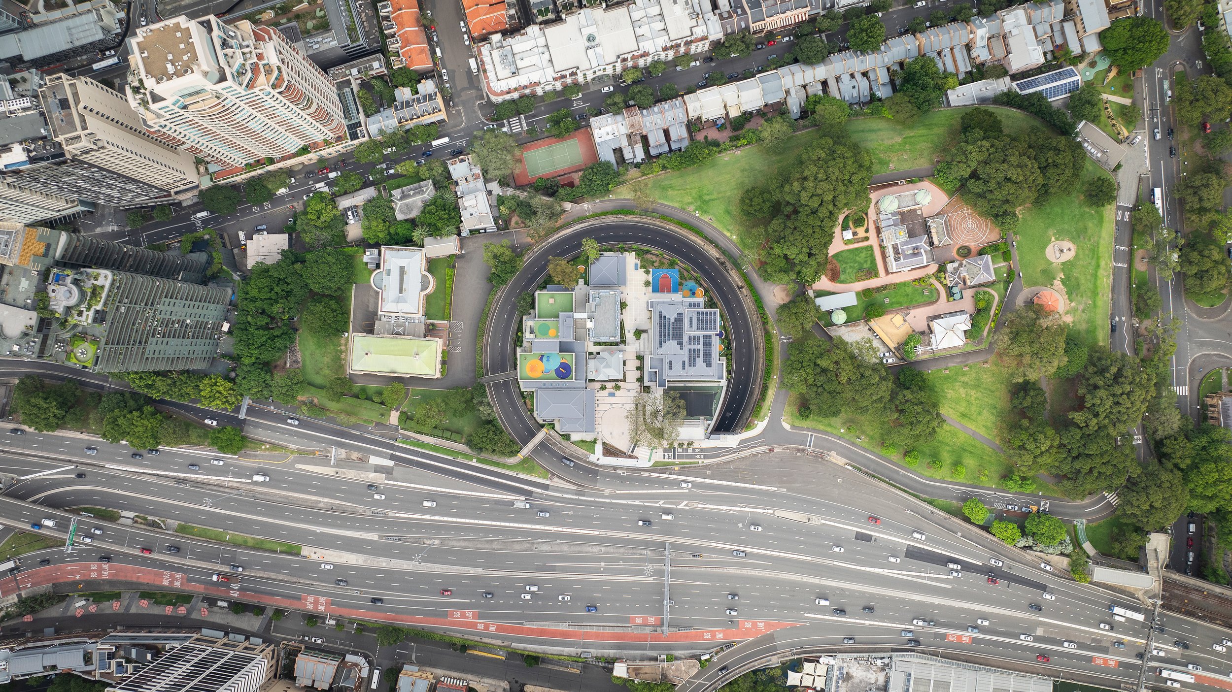 An aerial view of a city with a large road, several tall buildings, parks, and residential houses. Designed by fjcStudio Photo by Ruth Gold