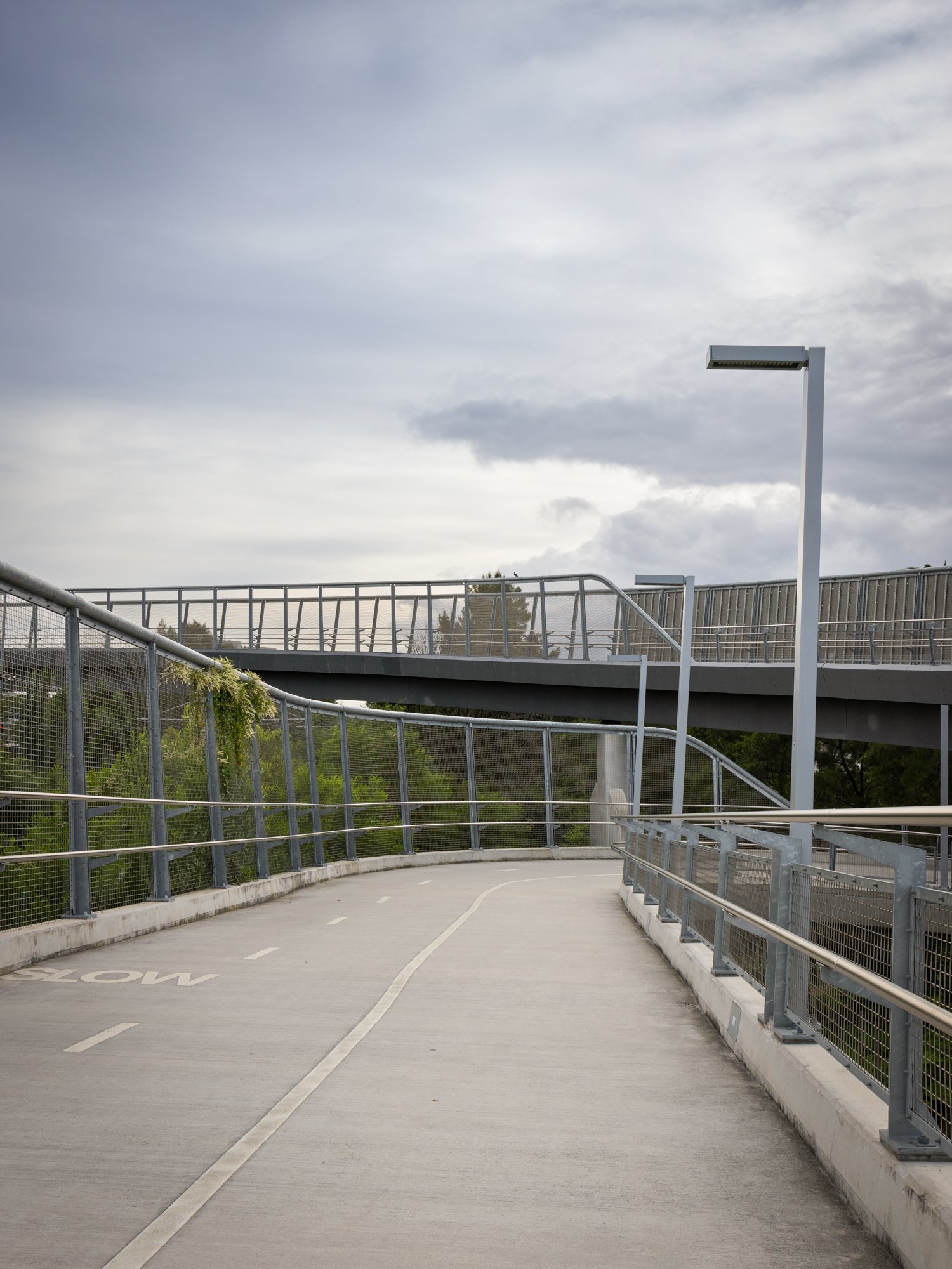 Empty outdoor parking garage ramp with metal railings, nearby trees, and cloudy sky. Designed by Colin Polwarth Studio Photo by Ruth Gold