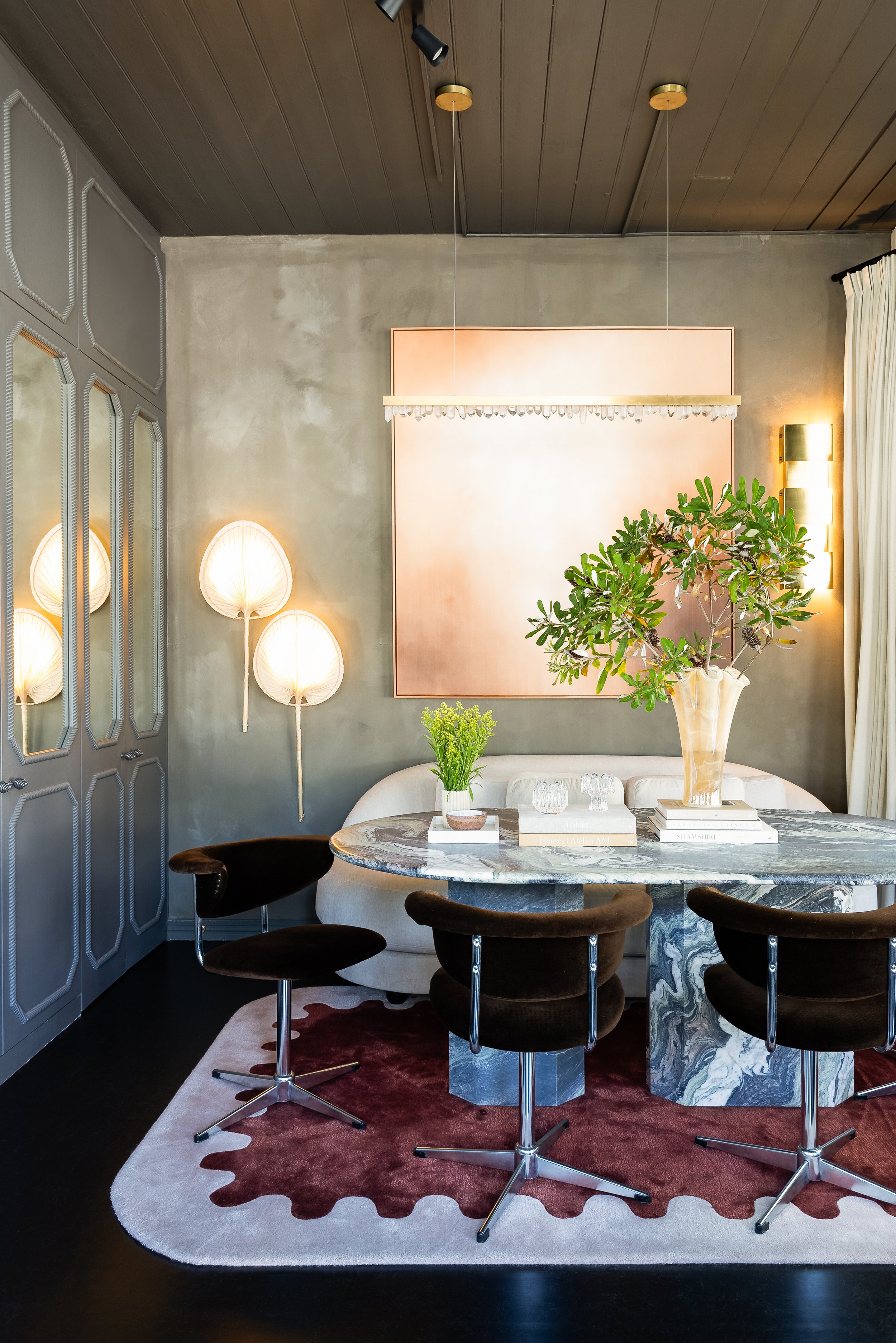 Modern dining room with a marble table, black chairs, a white sofa, and decorative lighting fixtures, including a large pink artwork on the wall and a green plant as a centerpiece. SMAC Studio Photo by Ruth Gold.