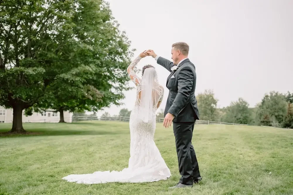 Bride and groom dancing outdoors on a grassy field with trees in the background.