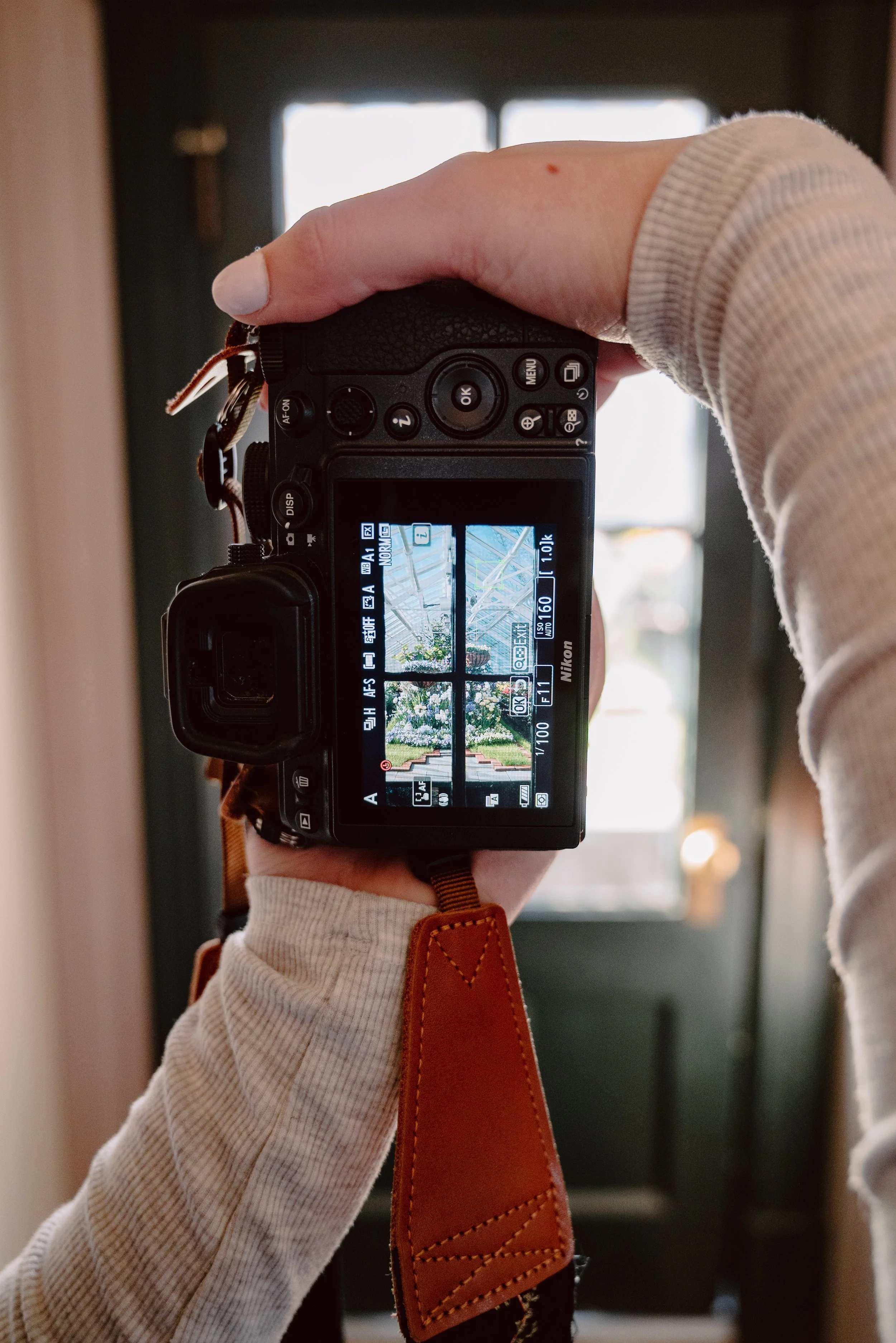 A person holding a Nikon camera, capturing a view of a garden with an archway and white flowers.